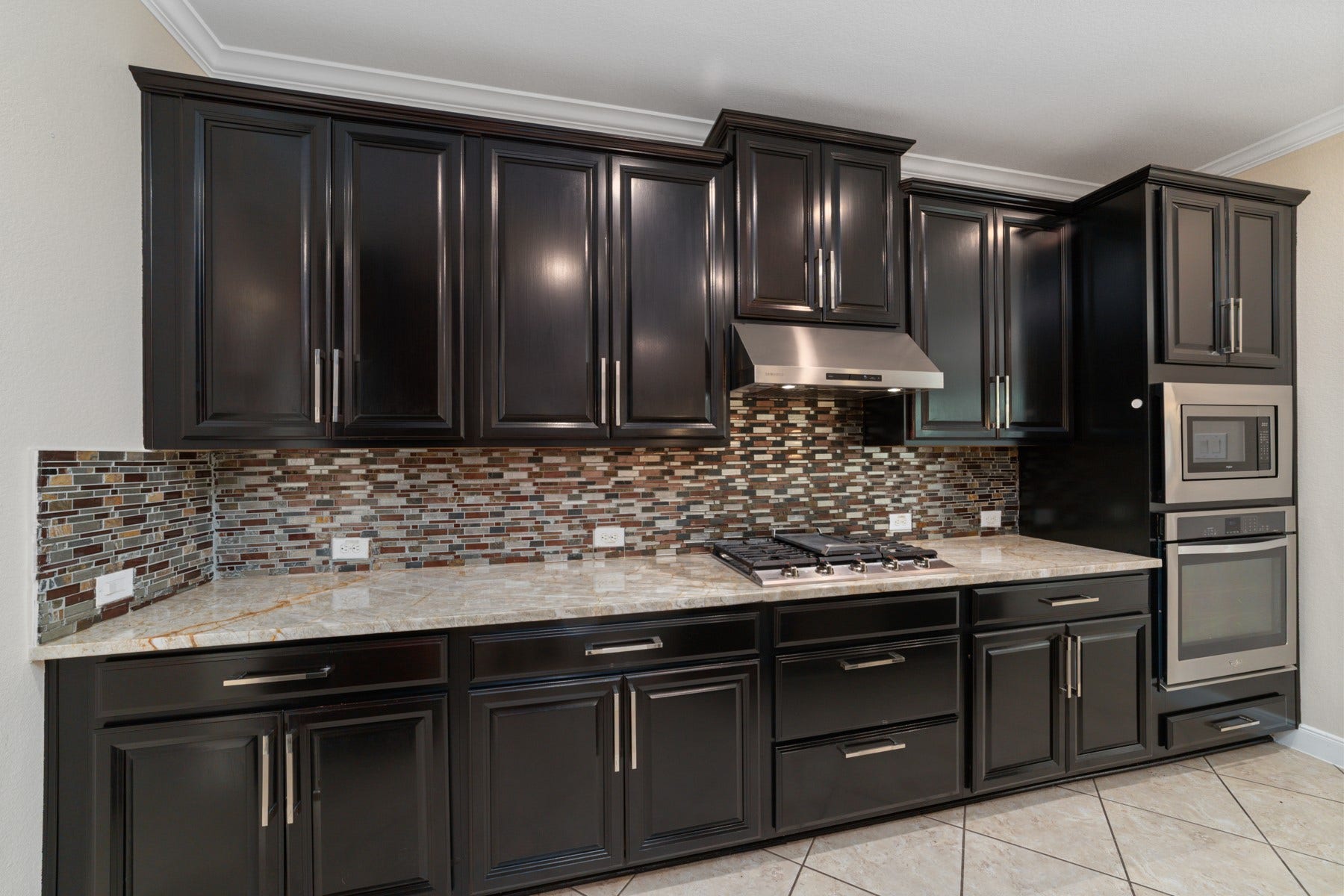 17302 Milrig Court, Richmond, TX 77407 Elegant kitchen featuring sleek dark cabinetry, stainless steel appliances, and a stylish mosaic tile backsplash, complemented by polished granite countertops.