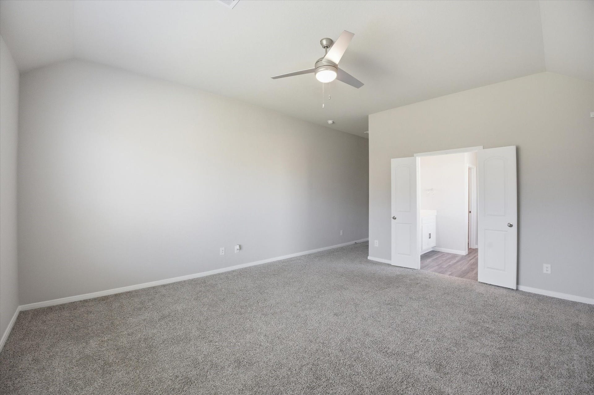 This spacious master bedroom features plush carpeting, a modern ceiling fan, and an inviting entrance to an en-suite bathroom, offering a perfect blend of comfort and style.