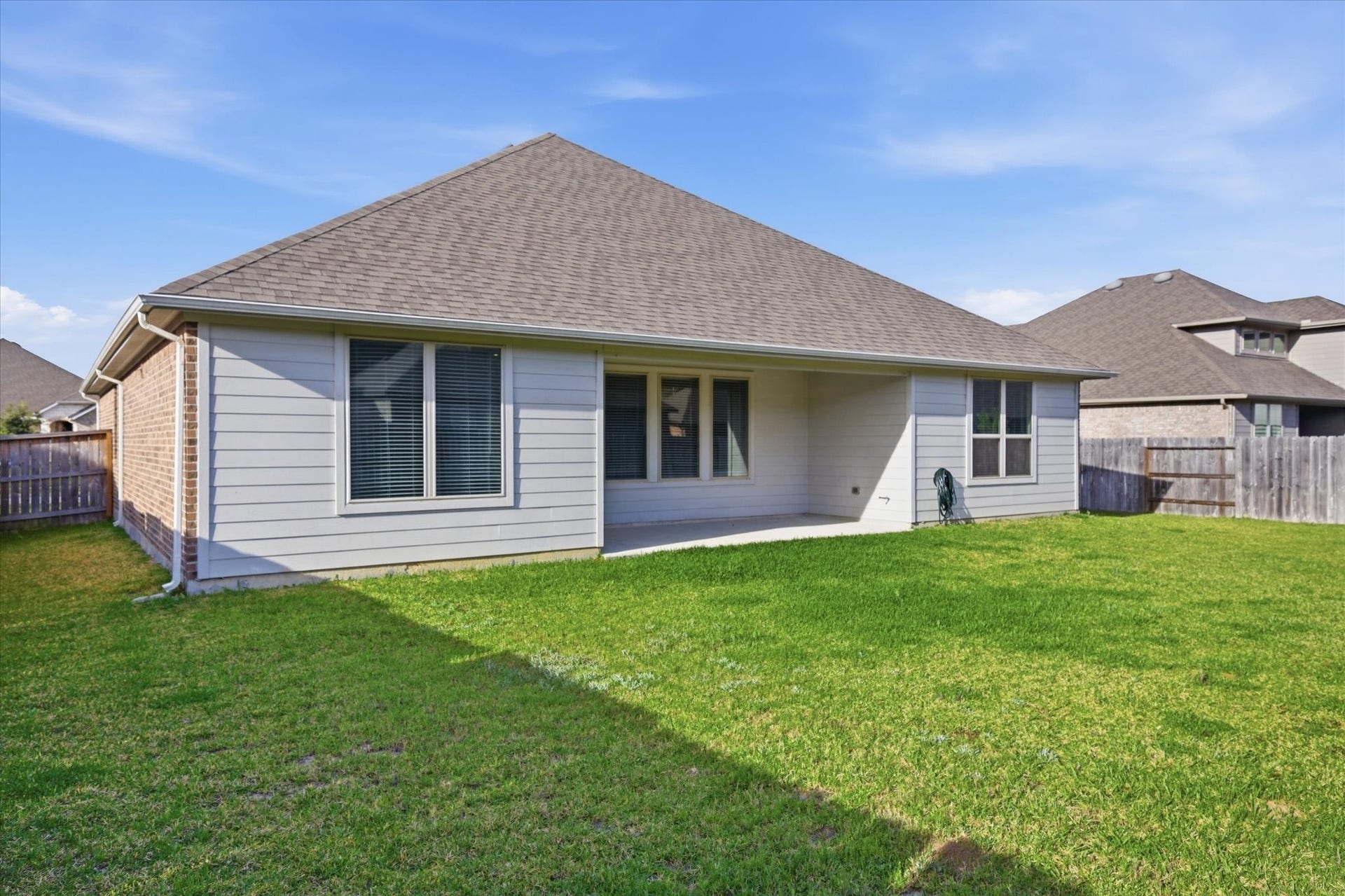 This photo shows the backyard of a single-story home with a spacious lawn, a covered patio, and a fenced boundary, perfect for outdoor activities and privacy.