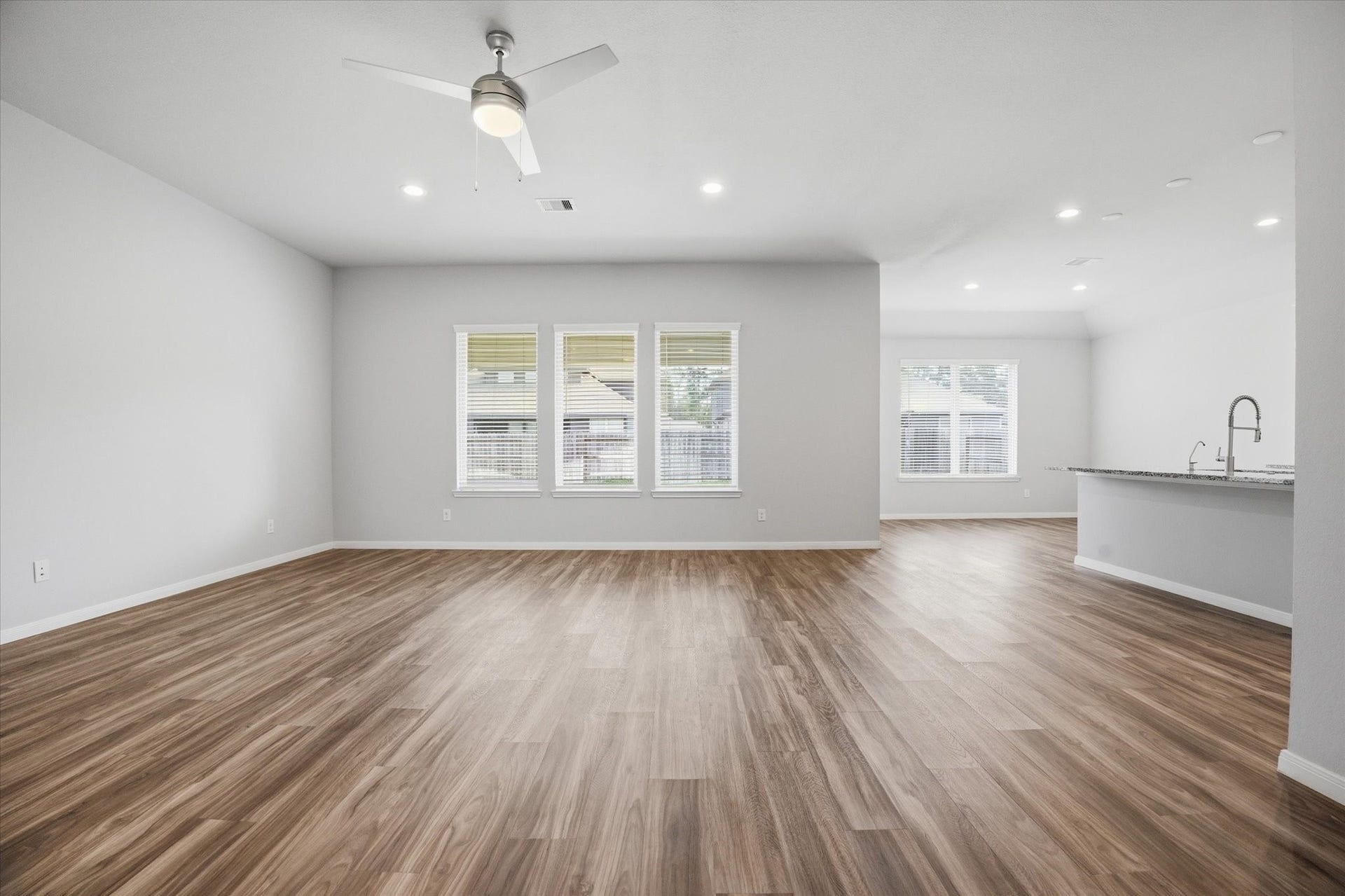 This spacious, carpeted room features neutral walls, a ceiling fan, and a large window providing ample natural light.