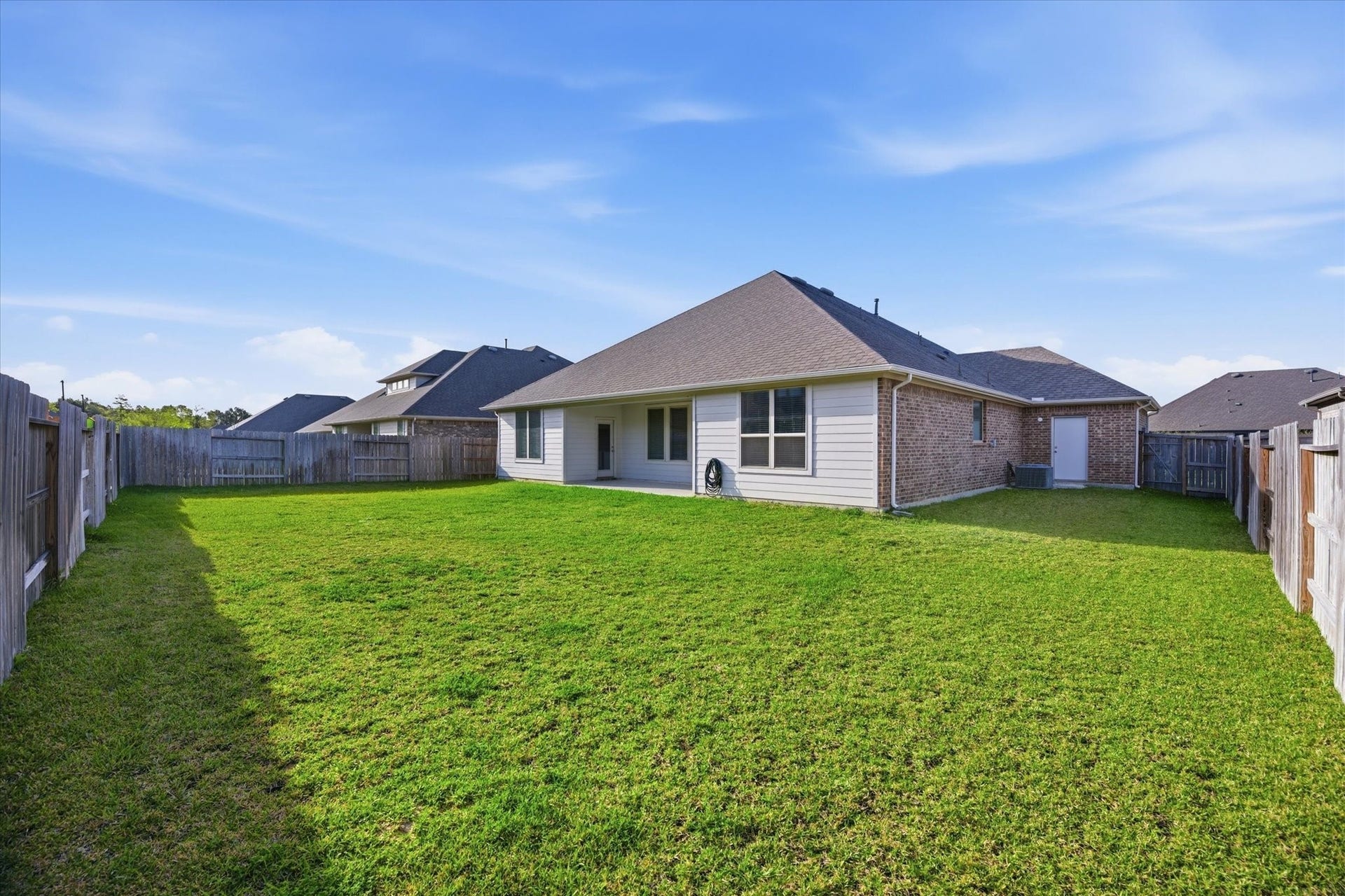 A spacious, fenced backyard with a well-maintained lawn and a modern, single-story brick house featuring large windows. Ideal for outdoor activities and privacy.