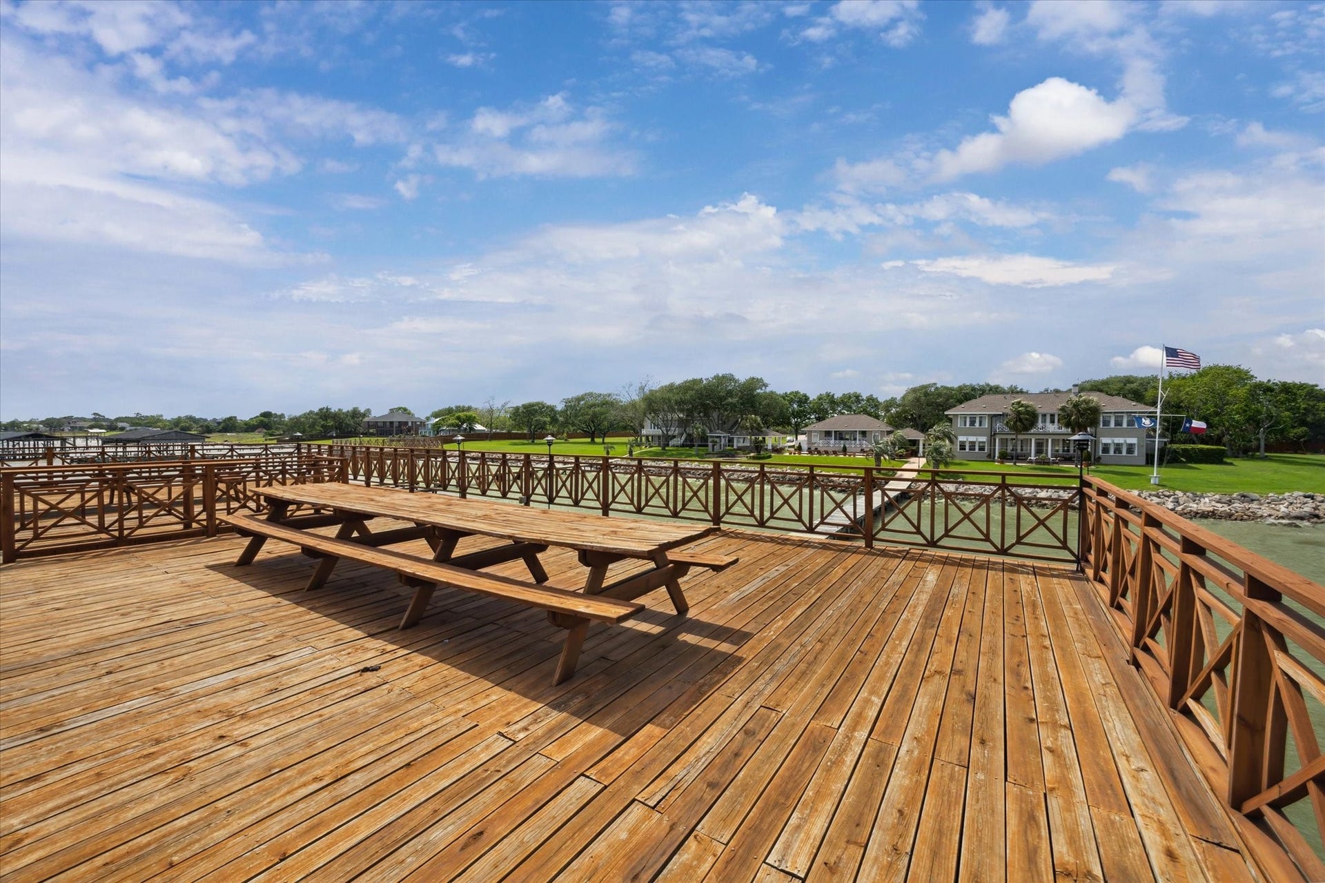 Expansive wooden deck overlooking a serene waterfront with a picnic table and views of nearby homes, perfect for outdoor relaxation and gatherings.