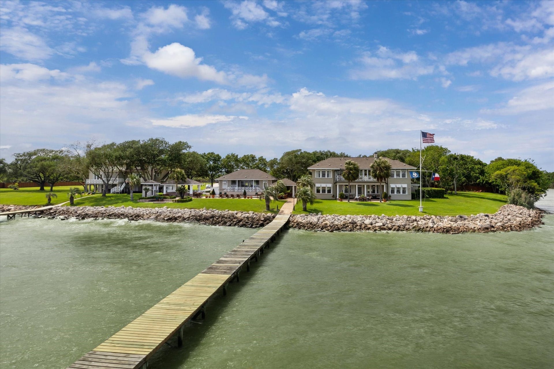 This waterfront property features a spacious home with a private dock extending into the water. The house is surrounded by lush greenery and a well-maintained lawn, offering scenic views and ample outdoor space. Perfect for those seeking a serene, picturesque setting.