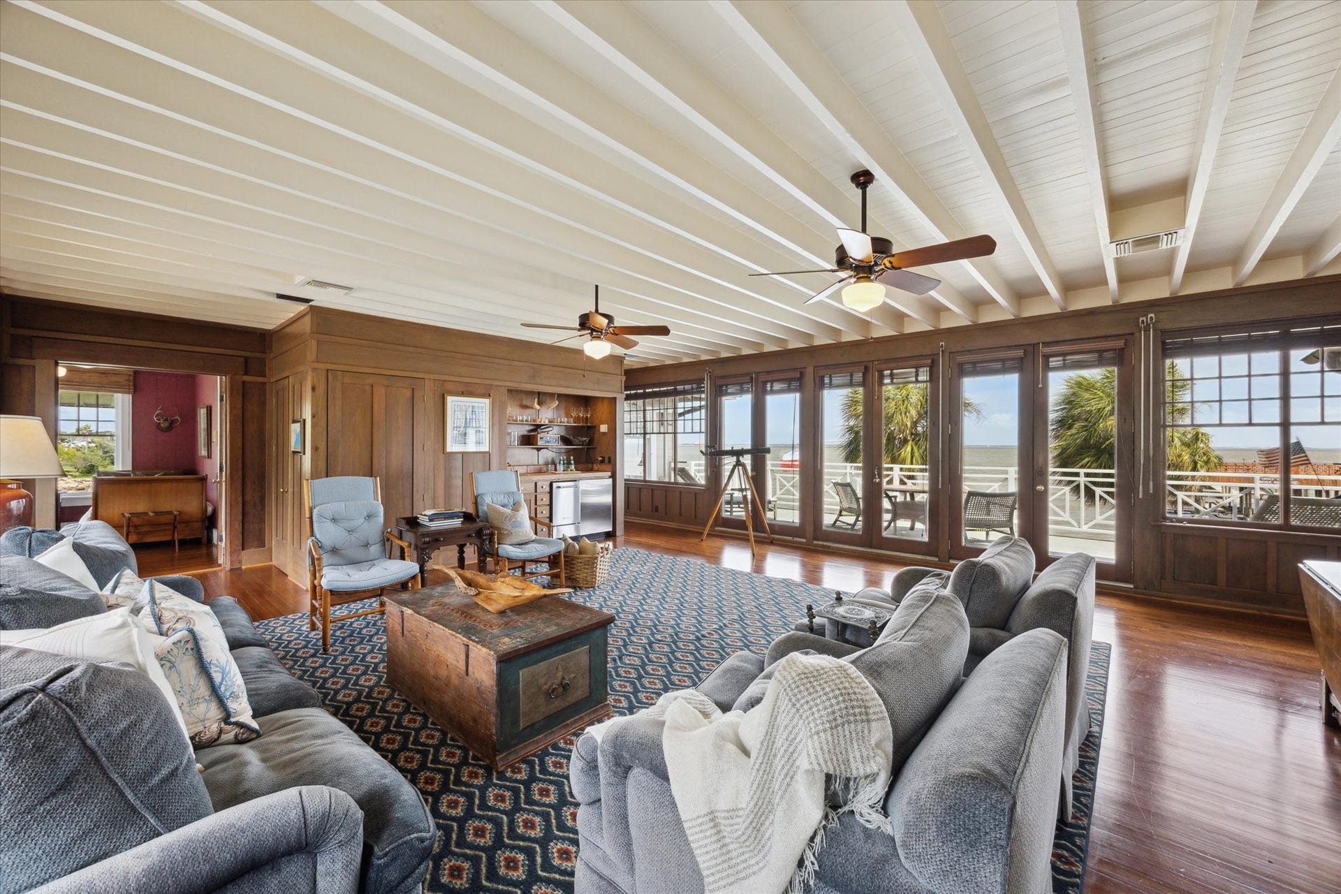 Second floor living room with expansive views of front lawn and bay with doors opening to large deck.