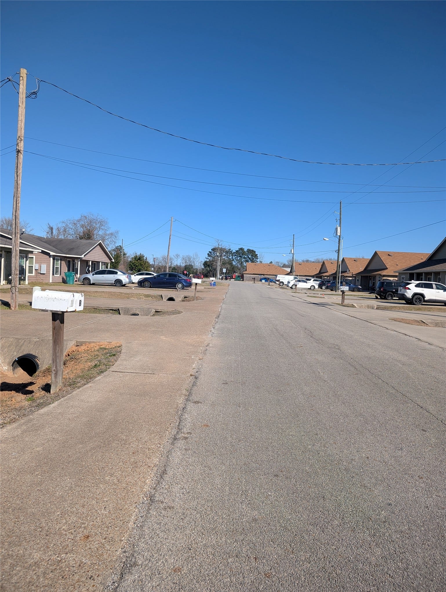 This photo shows a quiet residential street with single-story homes on both sides. The neighborhood appears well-maintained, with parked cars and clear skies indicating a peaceful setting. Perfect for a family-friendly environment.