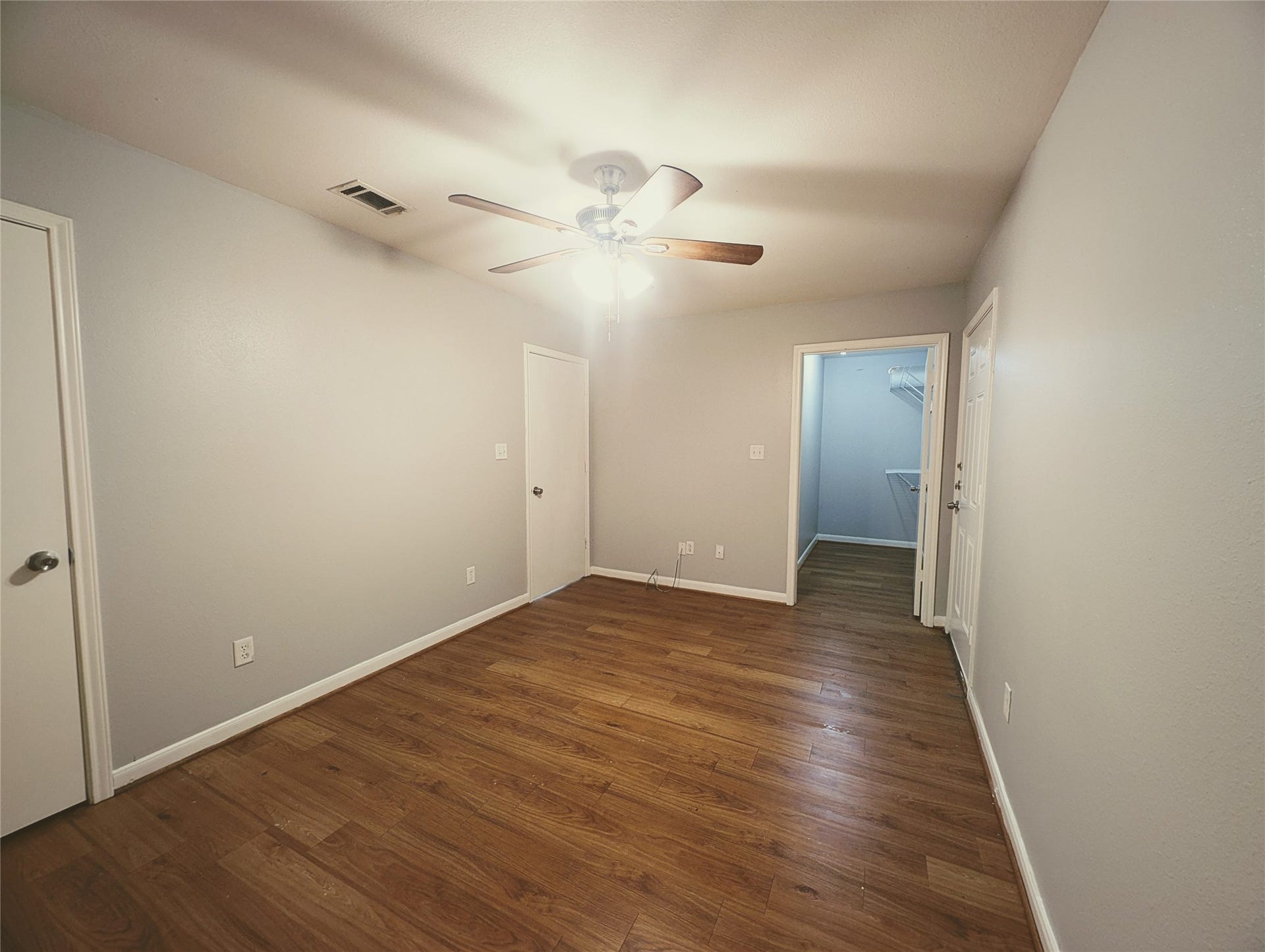This room features a neutral color palette with light gray walls and wood flooring. It includes a ceiling fan and offers access to a closet, creating a practical and comfortable space.
