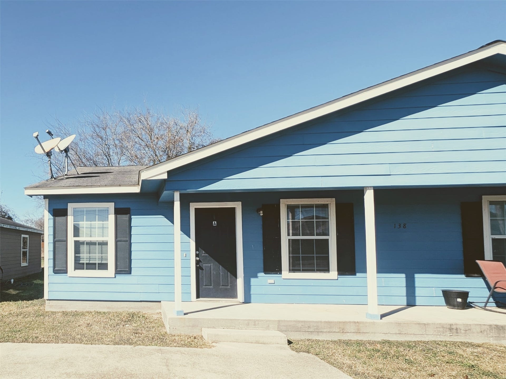 Charming single-story blue home with a covered porch and black shutters. Features a satellite dish on the roof and a well-maintained front yard. Ideal for buyers seeking a cozy and inviting property.