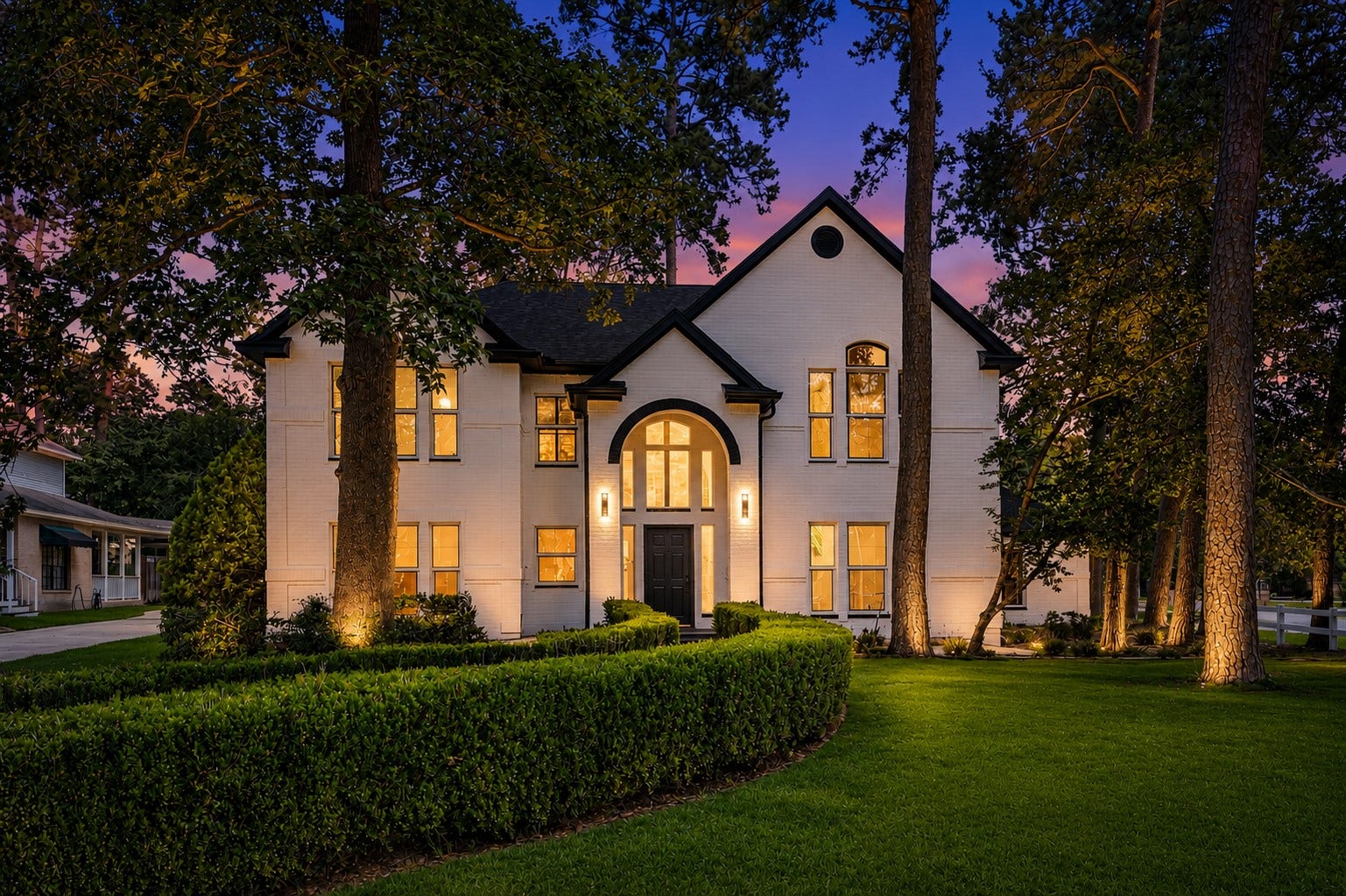 523 Rampart Lane, Conroe, TX 77302 Elegant two-story home with a striking white brick exterior, nestled among mature trees and lush greenery, featuring arched windows and a welcoming entryway. *Photo Digitally enhanced.