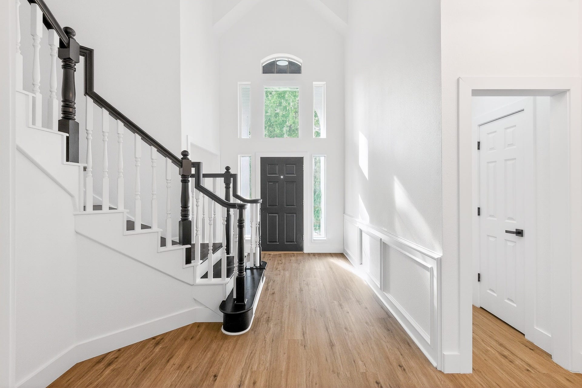 523 Rampart Lane, Conroe, TX 77302 Bright and inviting foyer with high ceilings, elegant staircase, and beautiful luxury vinyl flooring leading to a striking black front door.