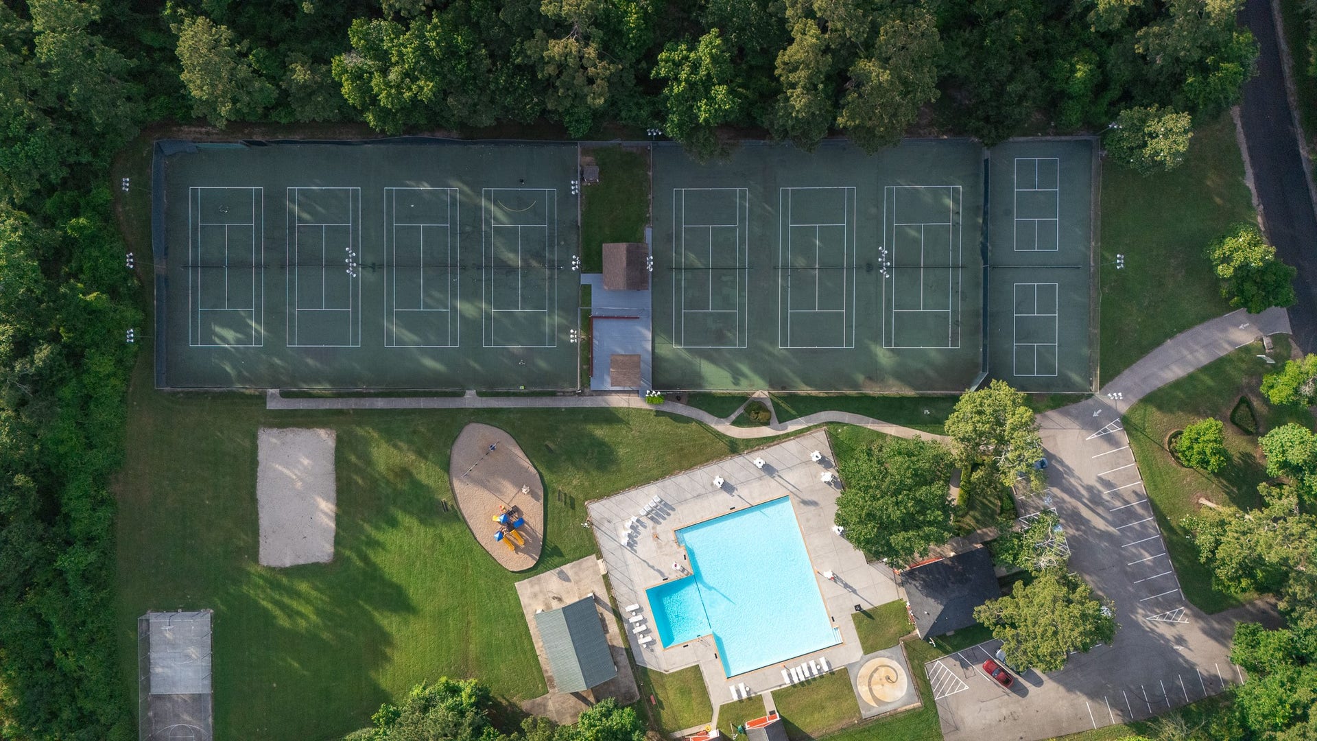 523 Rampart Lane, Conroe, TX 77302 This aerial view showcases a vibrant community recreation area featuring multiple tennis courts, a large swimming pool, a playground, and ample parking, all surrounded by lush greenery.
