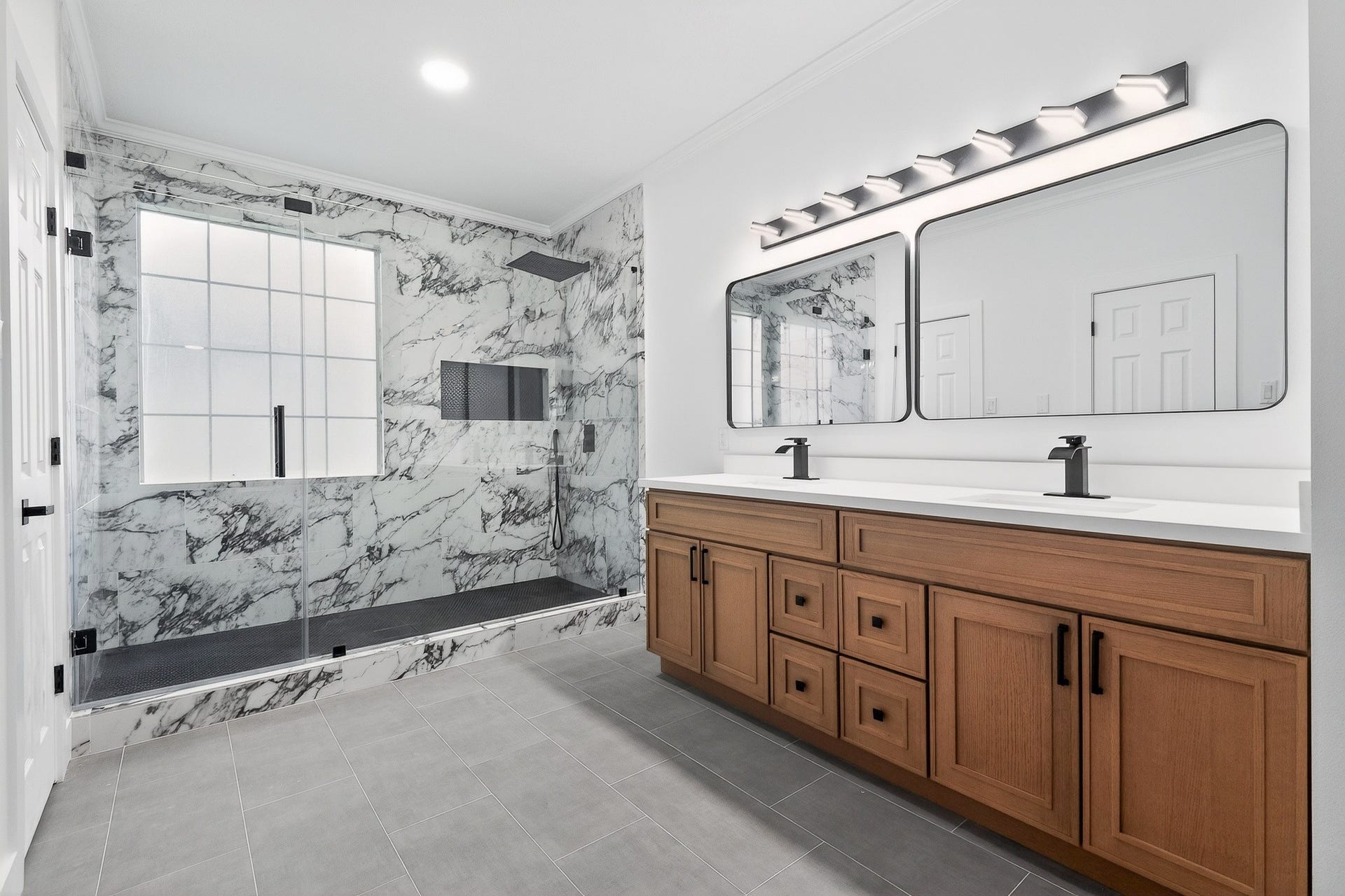 523 Rampart Lane, Conroe, TX 77302 Elegant bathroom featuring a spacious walk-in shower with marble-style walls, dual sinks with modern fixtures, and ample wooden cabinetry for storage.