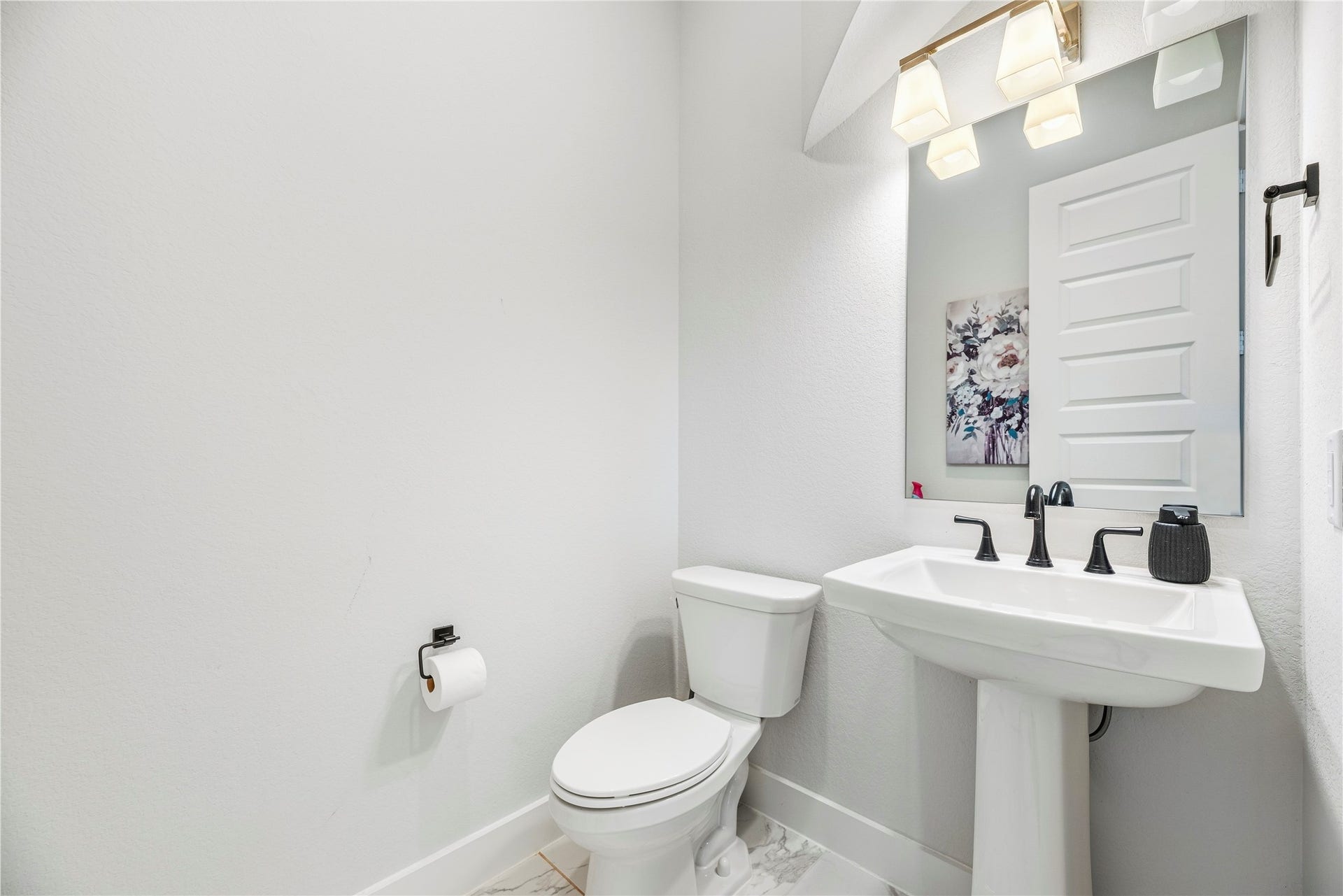 4810 Antler Run Drive, Spring, TX 77386 A bright, modern half-bathroom featuring a pedestal sink, sleek fixtures, and elegant lighting, complemented by a tasteful wall art piece.