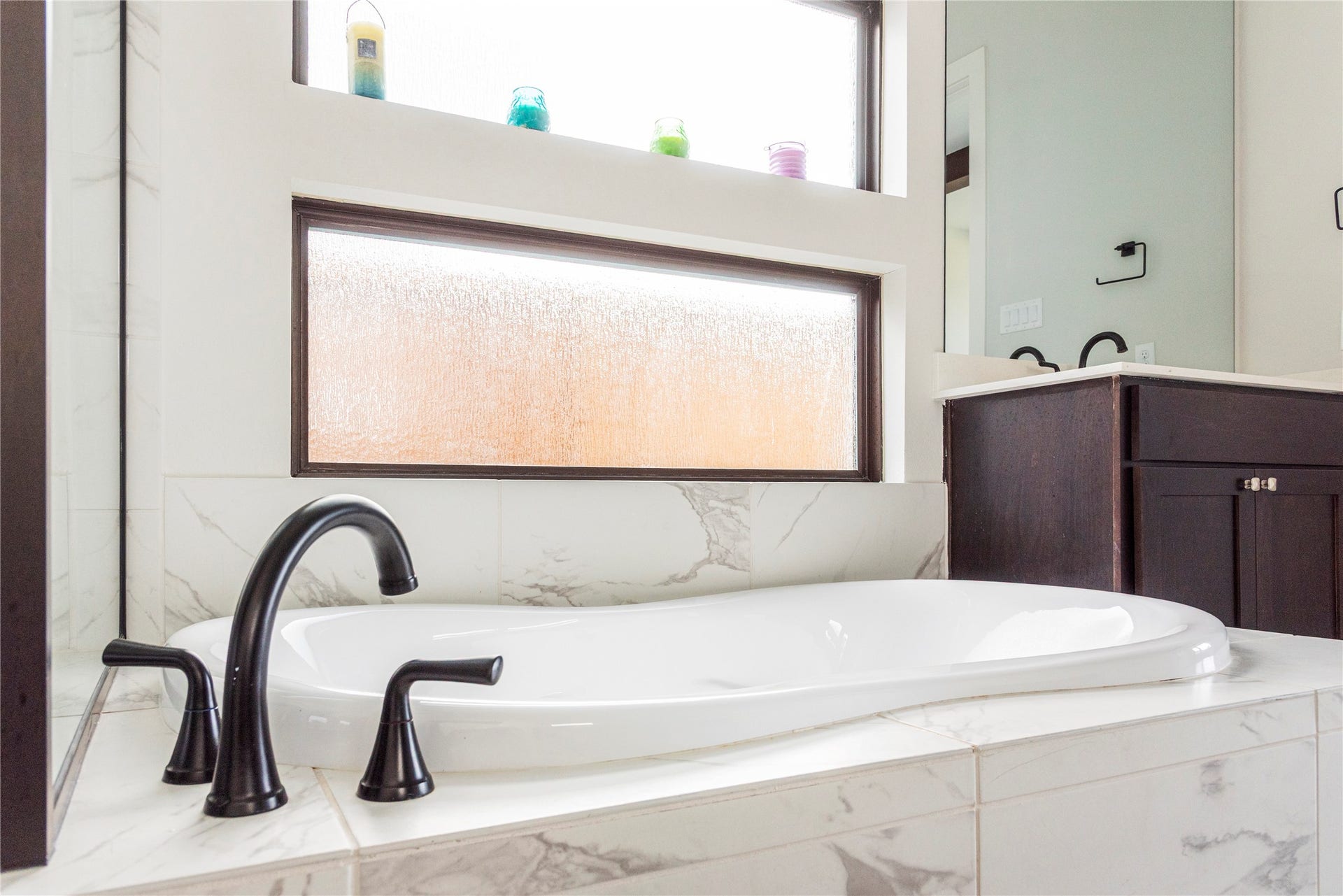 4810 Antler Run Drive, Spring, TX 77386 Elegant bathroom featuring a luxurious soaking tub with sleek black fixtures, set against a backdrop of marble tile and frosted windows for privacy.