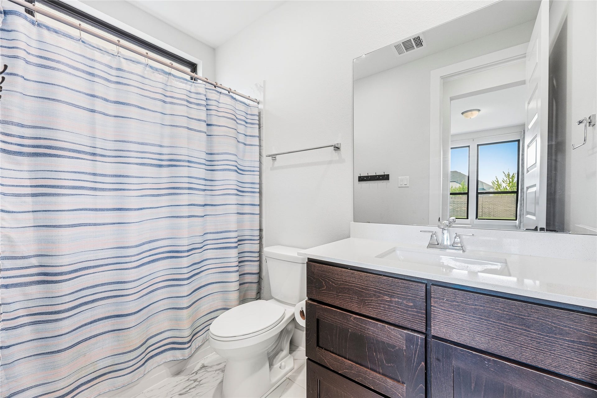 4810 Antler Run Drive, Spring, TX 77386 Bright and modern bathroom featuring a sleek vanity with dark wood cabinetry, a spacious mirror, and a bathtub with a striped shower curtain.