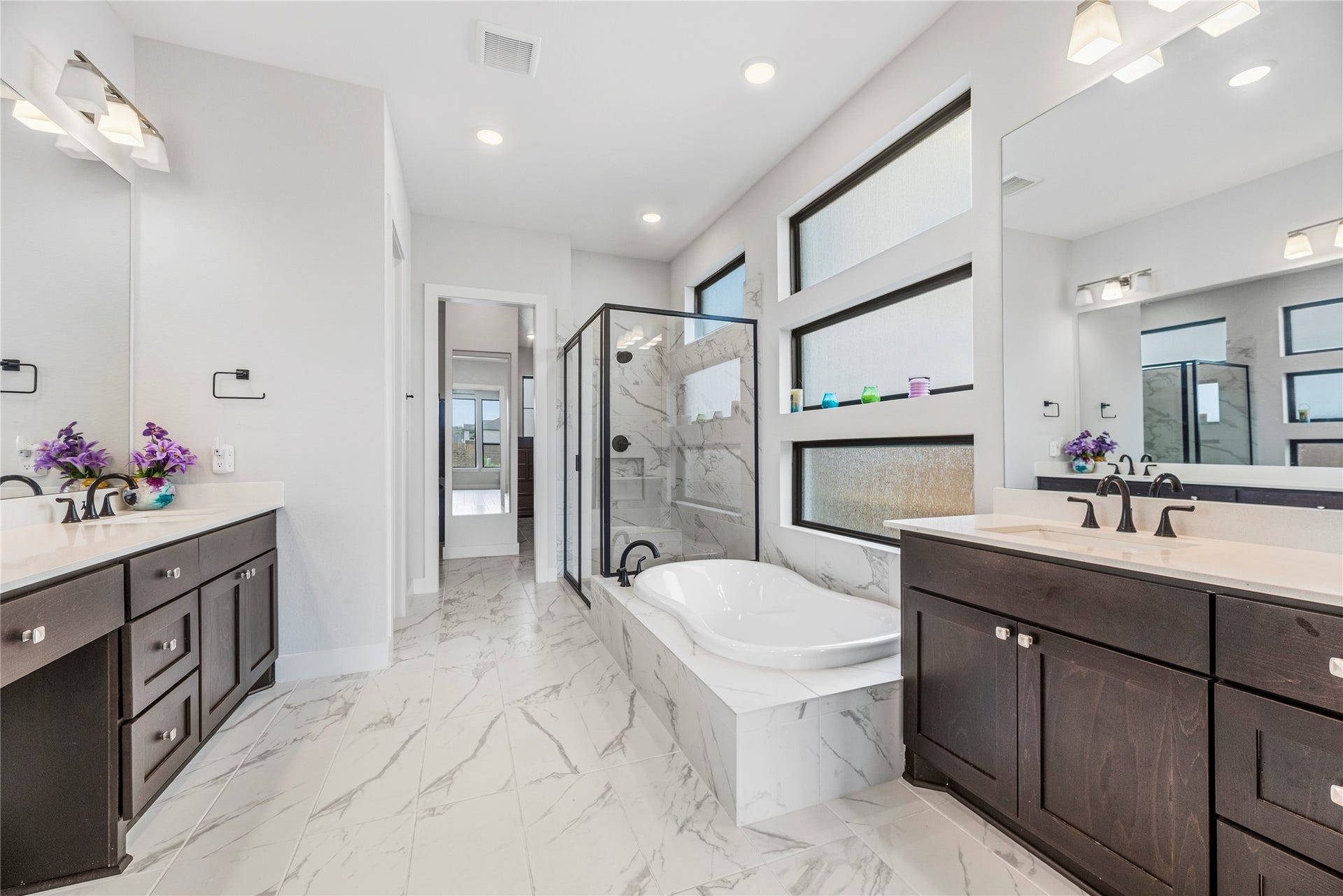 4810 Antler Run Drive, Spring, TX 77386 Luxurious bathroom featuring a modern freestanding tub, spacious walk-in shower with glass enclosure, dual vanities with dark wood cabinetry, and sleek marble flooring.