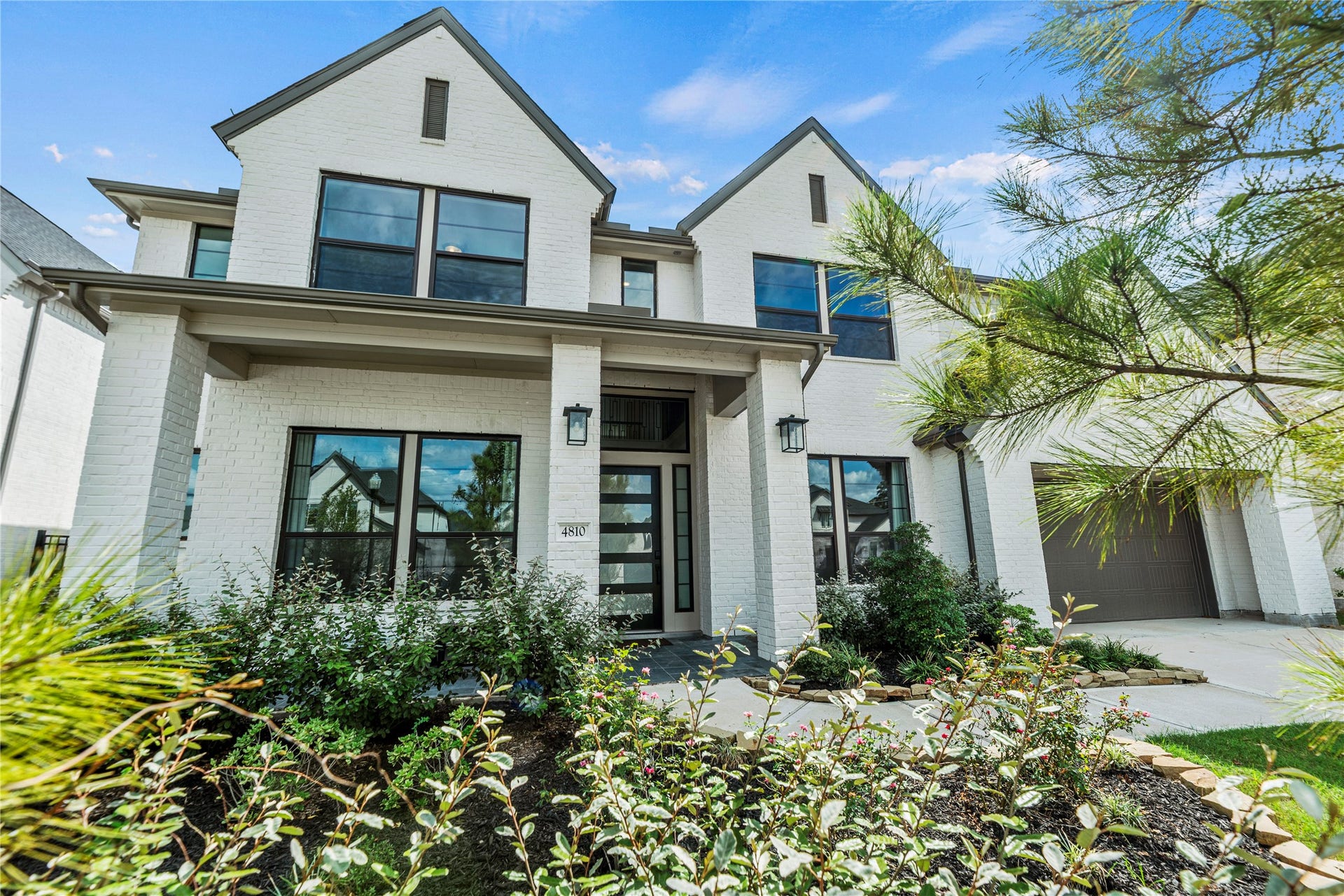 4810 Antler Run Drive, Spring, TX 77386 Stunning modern home with a crisp white brick exterior, charming gabled rooflines, and a beautifully landscaped front yard, offering excellent curb appeal.