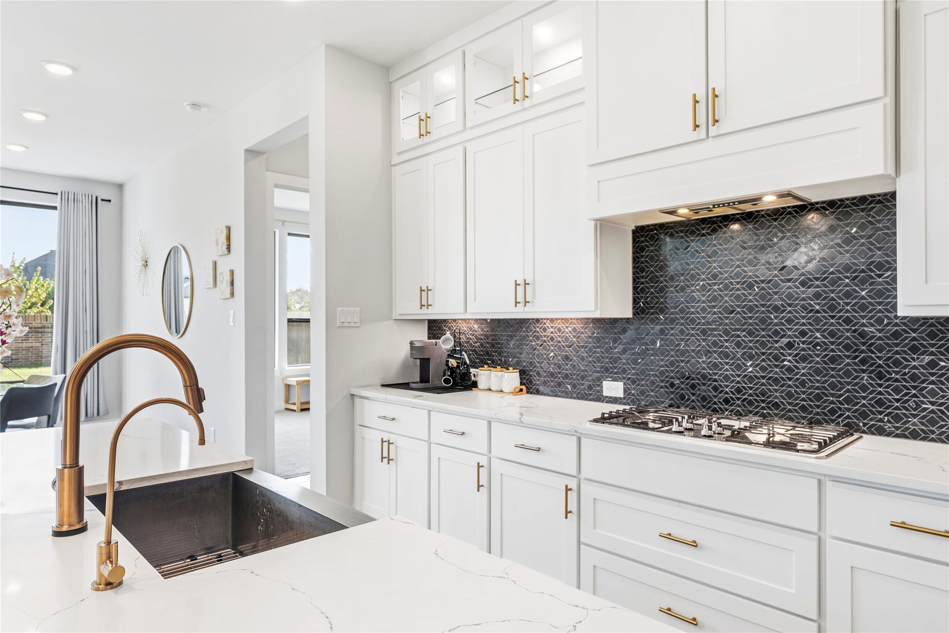 4810 Antler Run Drive, Spring, TX 77386 Sleek and modern kitchen featuring white cabinetry, a striking dark geometric backsplash, and a spacious island with a stylish bronze faucet. Bright and airy with ample natural light.