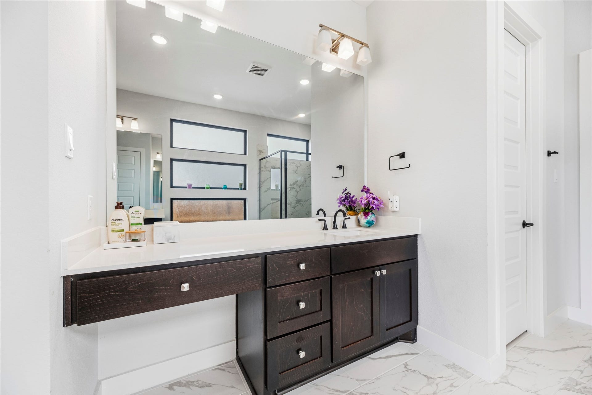 4810 Antler Run Drive, Spring, TX 77386 Elegant bathroom with a sleek dark wood vanity, modern fixtures, and a large mirror, complemented by bright lighting and stylish tile flooring.