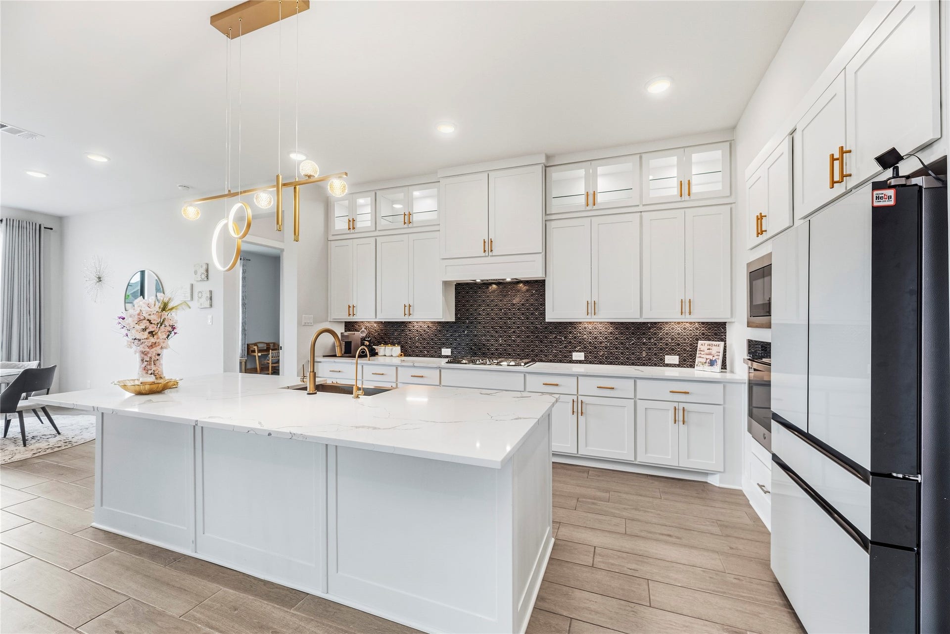 4810 Antler Run Drive, Spring, TX 77386 Crisp kitchen featuring sleek white cabinetry, a spacious marble island with elegant gold fixtures, and a striking dark backsplash. High end Refrigerator matches perfectly and comes with the property!