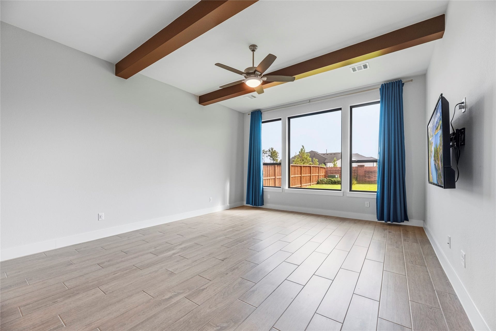 4810 Antler Run Drive, Spring, TX 77386 Spacious room featuring elegant wood-look tile flooring, exposed ceiling beams, and large windows with vibrant blue drapes offering a view of the backyard.