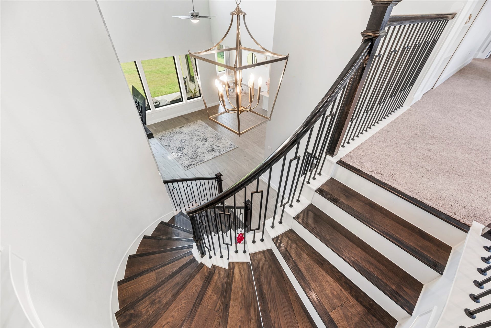 4810 Antler Run Drive, Spring, TX 77386 Elegant curved staircase with dark wood steps and sleek black railings, highlighted by a grand chandelier and open view to the living area below.