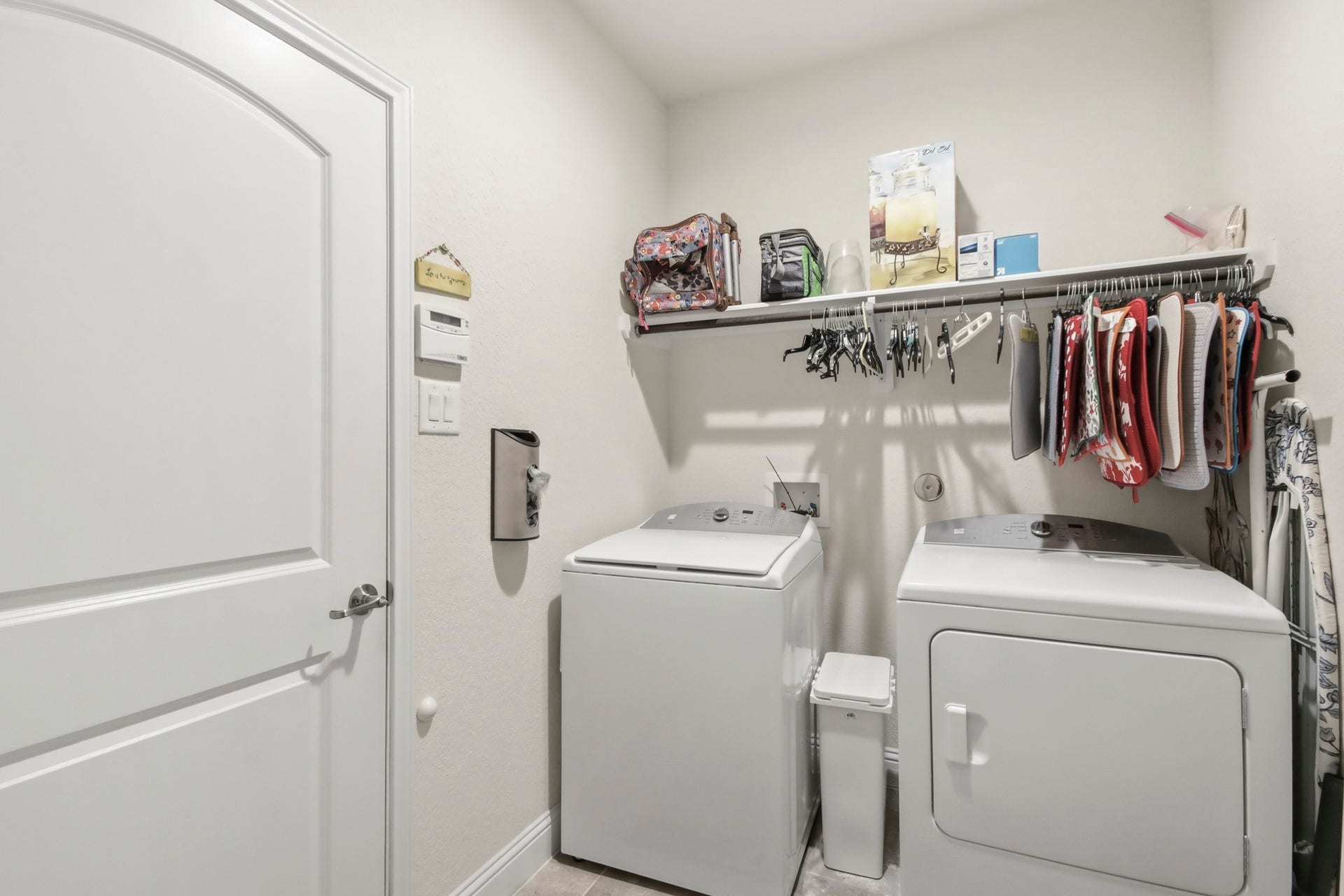 11 Whispering Thicket Place, The Woodlands, TX 77375 Spacious laundry room featuring a washer and dryer, ample shelving for storage, and convenient access from both the hallway near the kitchen and the garage.