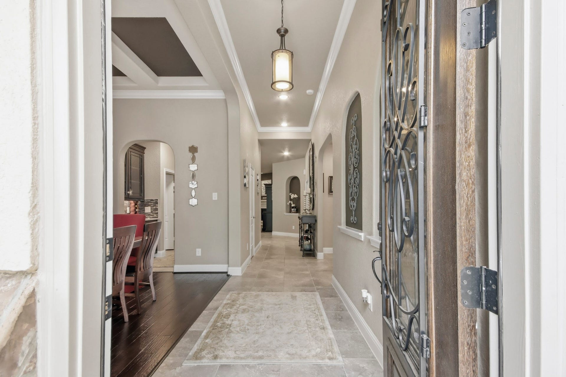 11 Whispering Thicket Place, The Woodlands, TX 77375 Elegant entryway featuring a decorative iron door, high ceilings, and a well-lit corridor leading to a spacious dining area with rich wood flooring.
