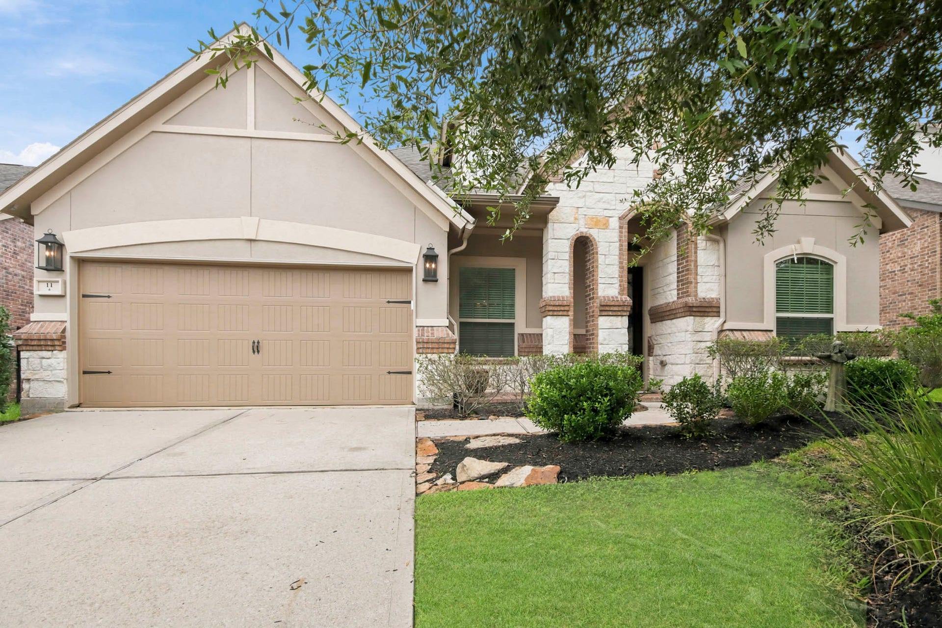 11 Whispering Thicket Place, The Woodlands, TX 77375 Beautiful 1.5-story home built by Ryland Homes with a welcoming front facade featuring a blend of stone/brick and stucco accents, a spacious two-car garage, and landscaped greenery.