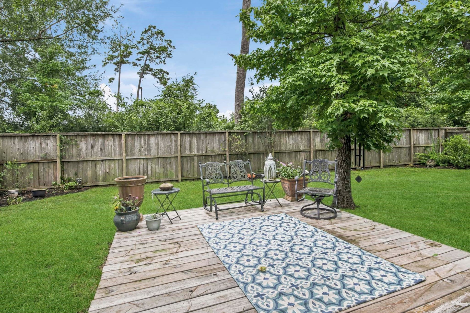 11 Whispering Thicket Place, The Woodlands, TX 77375 Backyard features a beautiful wooden deck with stylish seating, surrounded by lush greenery and a privacy fence, creating the perfect setting for relaxation and outdoor gatherings.