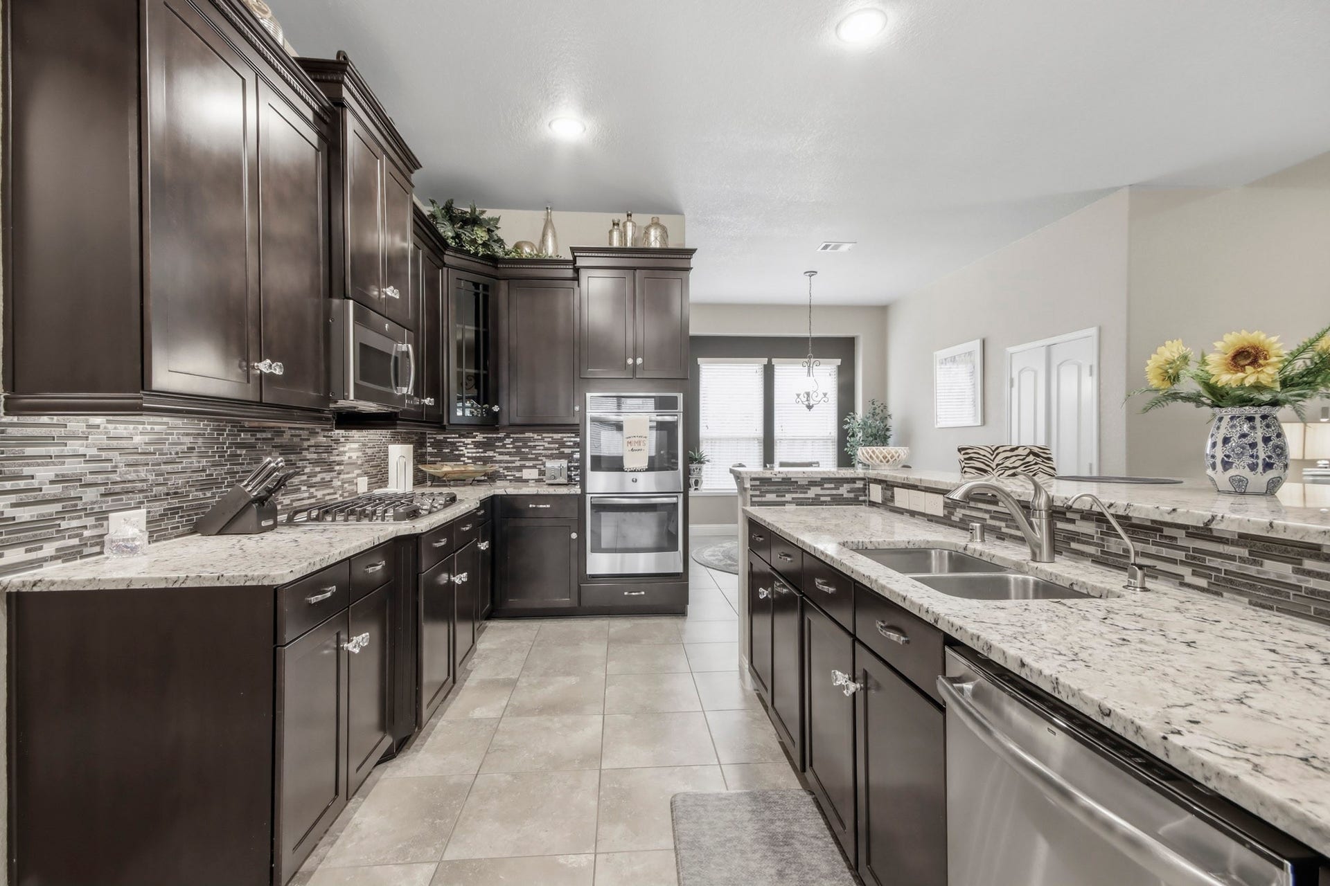 11 Whispering Thicket Place, The Woodlands, TX 77375 Chef-grade kitchen featuring rich dark wood cabinetry, stainless steel appliances, and a spacious granite countertop with dual sinks.
