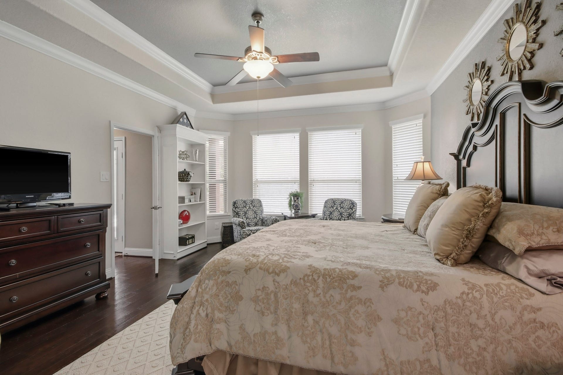 11 Whispering Thicket Place, The Woodlands, TX 77375 Stylish Primary Suite with tray ceiling, large windows with a cozy seating area and rich wood flooring.