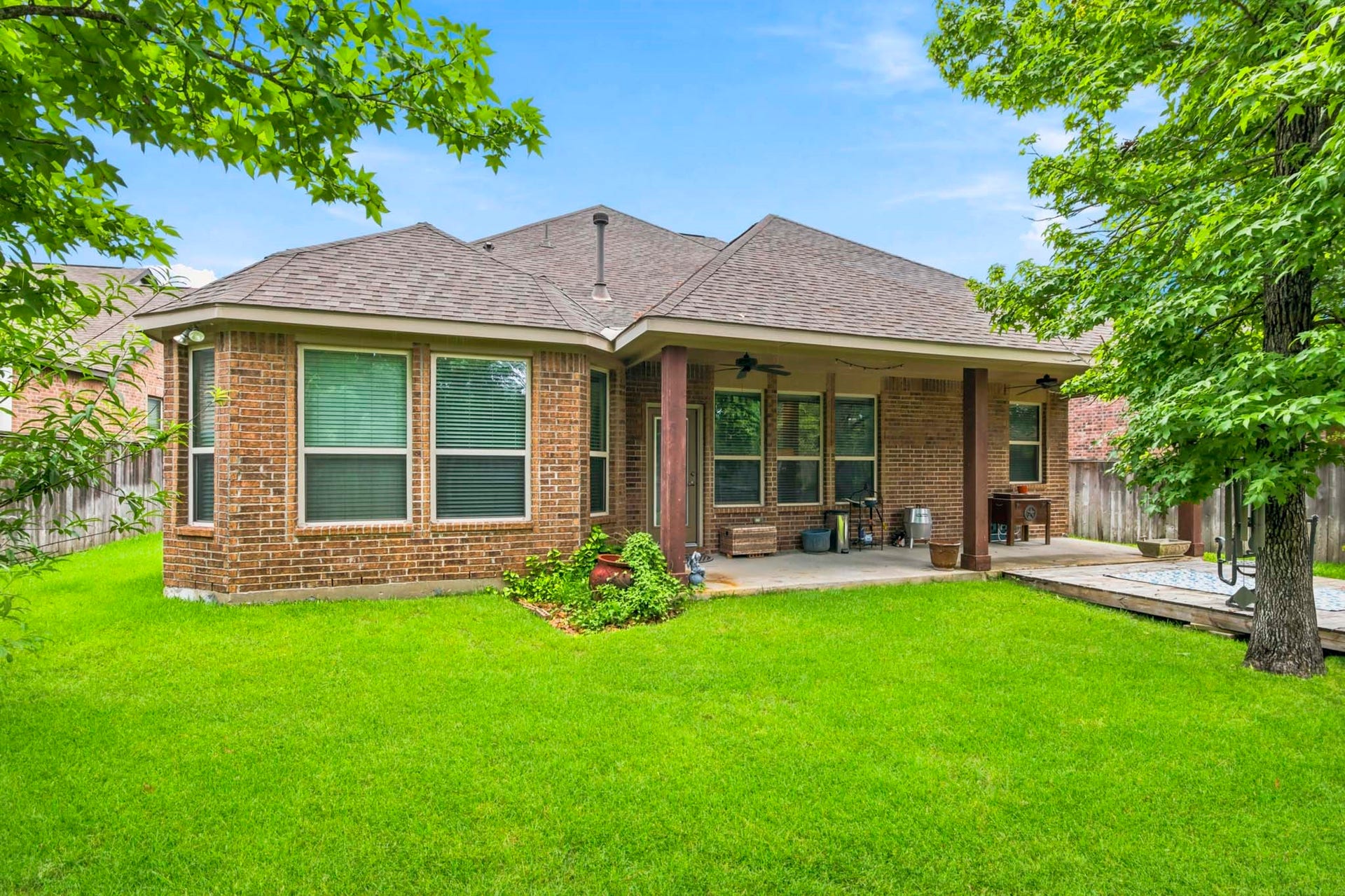 11 Whispering Thicket Place, The Woodlands, TX 77375 Rear view of the spacious backyard featuring a covered patio, perfect for outdoor relaxation and entertaining, surrounded by lush greenery.