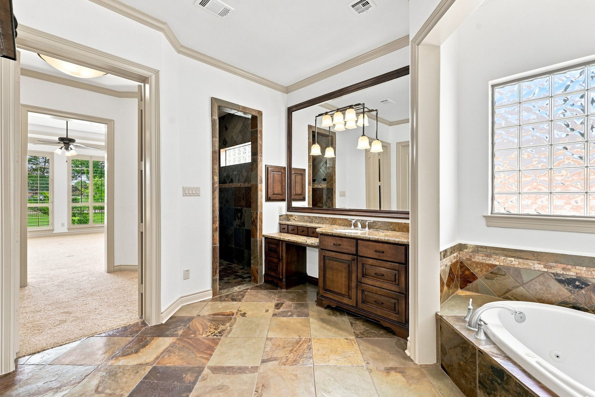 5411 Woodbury Street, Fulshear, TX 77441 This view showcases the entrance to the spacious walk-in shower, beautifully finished with floor-to-ceiling slate tile. Looking back toward the Primary Bedroom, the view highlights the seamless flow between the luxurious bath and private bedroom retreat.