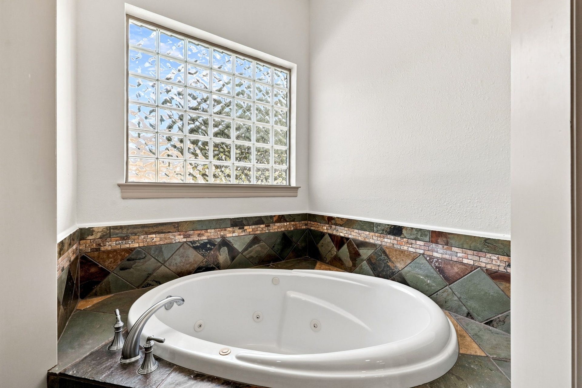 5411 Woodbury Street, Fulshear, TX 77441 The luxurious jetted tub is perfectly positioned beneath a wall of elegant block-glass windows, allowing natural light to filter into the space while maintaining privacy. A beautiful slate-tile surround completes the sophisticated look, creating a relaxing focal point within the Primary Bathroom.