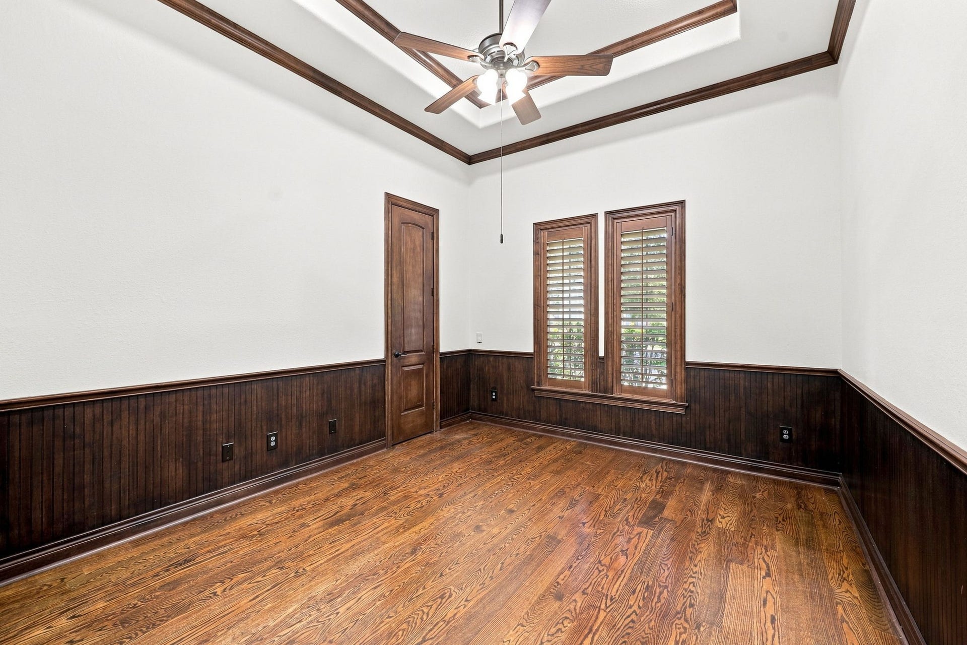 5411 Woodbury Street, Fulshear, TX 77441 The spacious home office is beautifully appointed with rich wood flooring, a dramatic raised ceiling accented by detailed crown molding, and elegant wainscoting. Plantation shutters frame the windows, adding timeless sophistication while providing privacy and natural light. A generously sized storage closet completes this exceptional and highly functional workspace.