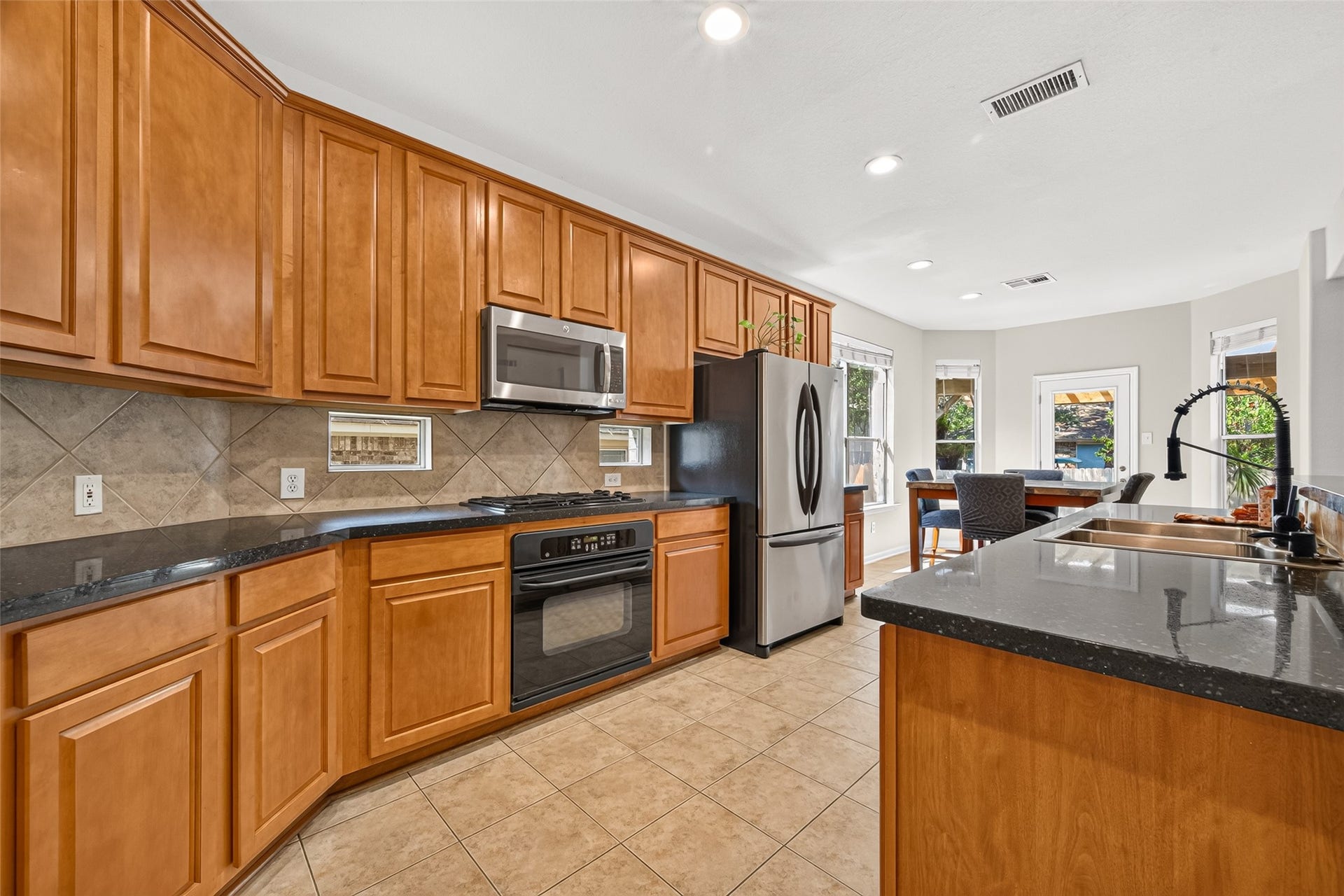 Spacious kitchen featuring abundant cabinetry, generous counter space, stainless steel appliances, and a convenient breakfast area overlooking the backyard.