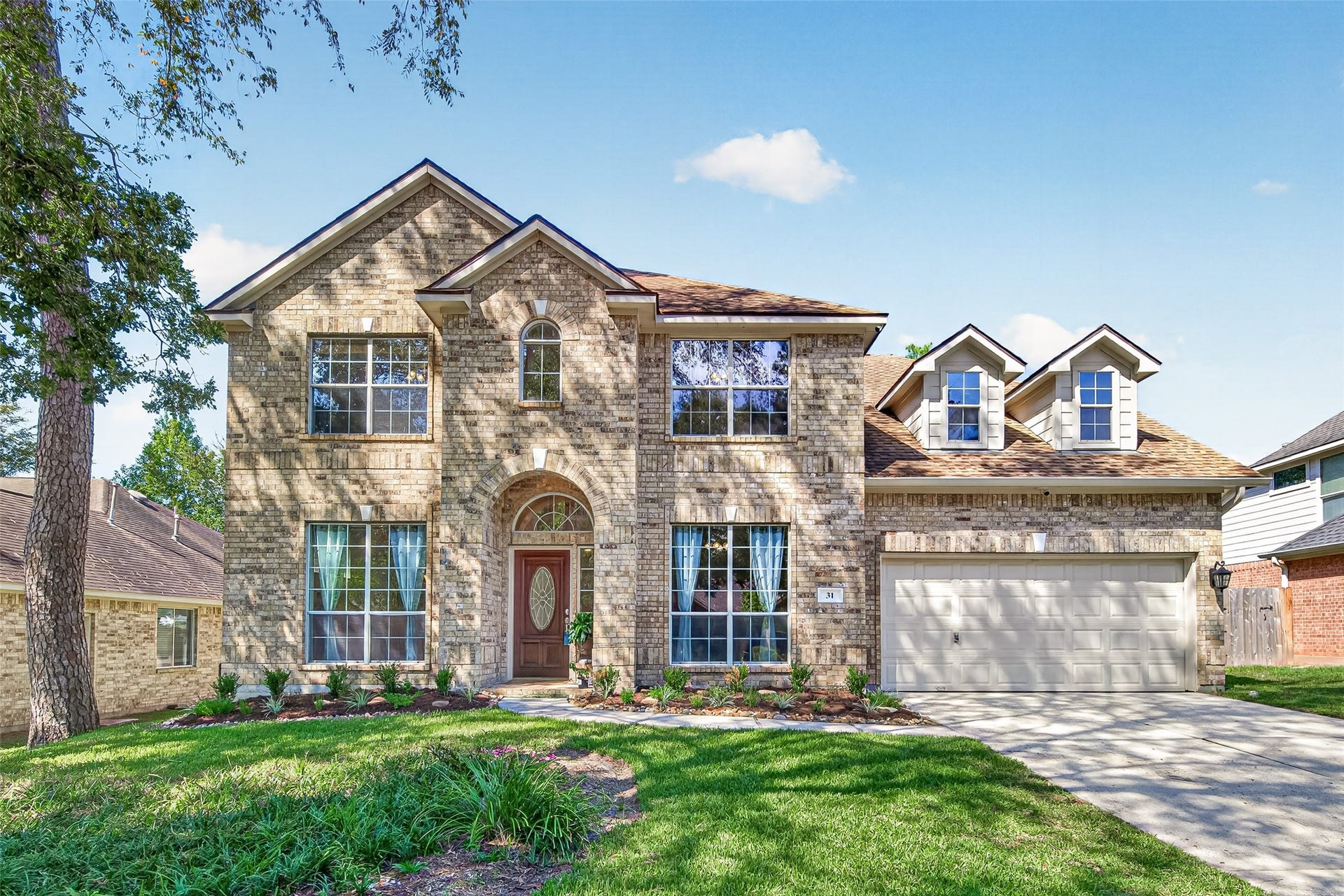 Beautiful two-story brick home featuring timeless curb appeal, a welcoming arched entryway, large windows, mature trees, manicured landscaping, and a spacious two-car garage.