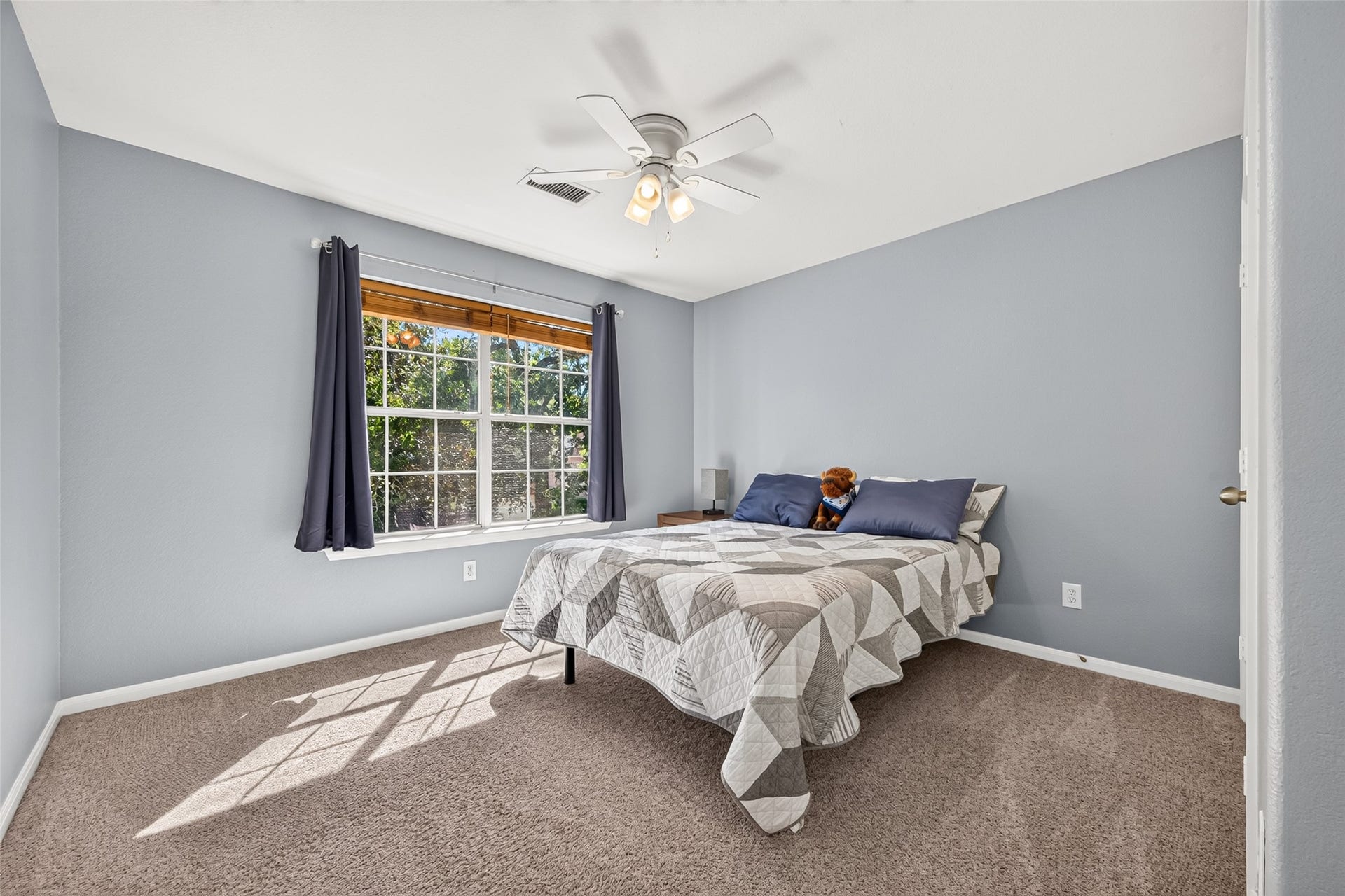 Bright and inviting secondary bedroom featuring a large window, ceiling fan, and neutral carpeting.