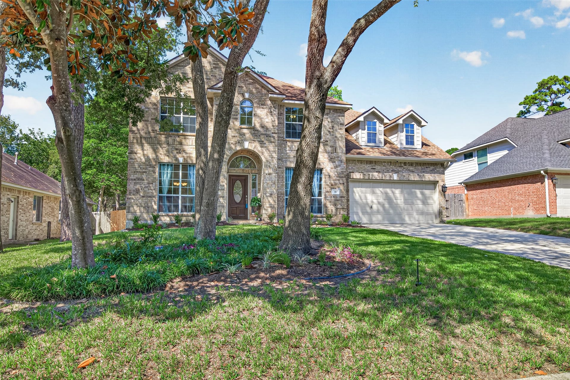 Beautiful curb appeal surrounded by mature shade trees, lush greenery, and thoughtfully landscaped flower beds.