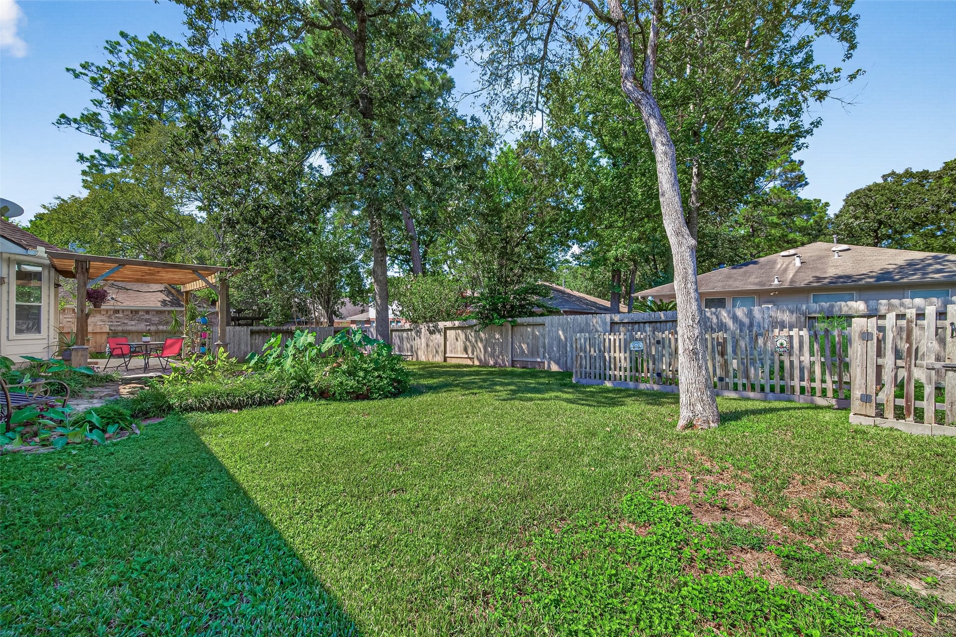 Spacious, tree-shaded backyard featuring a dedicated fenced garden area, perfect for growing vegetables, herbs, or flowers.