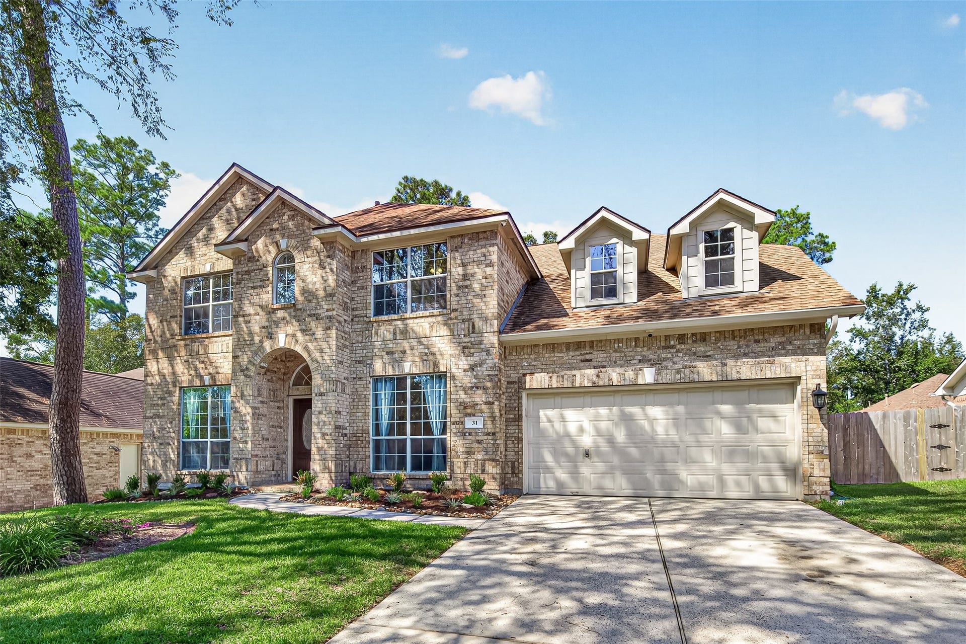 Another beautiful view showcasing the home's classic brick exterior, distinctive dormer windows, spacious driveway, and two-car garage.