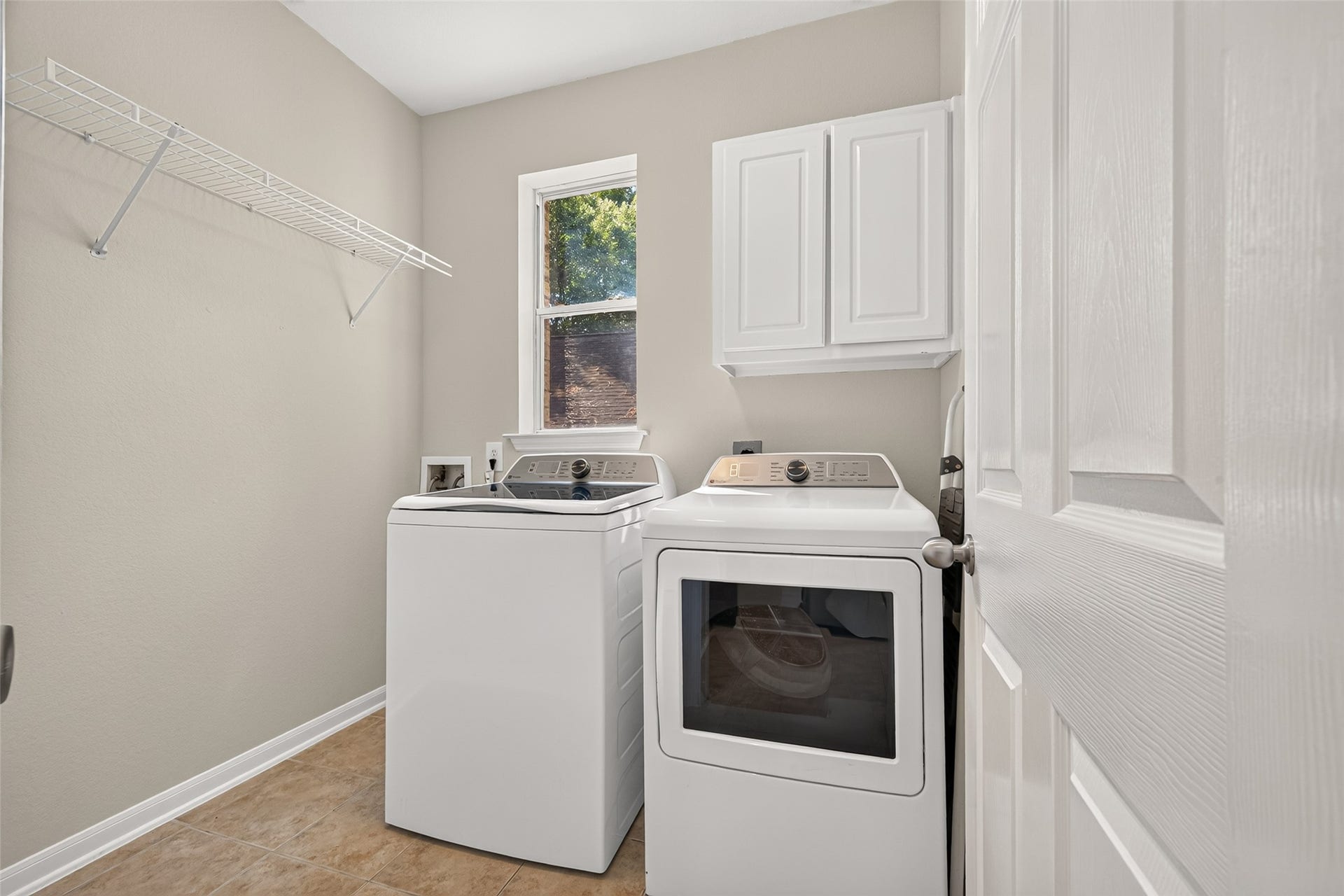Spacious utility room with built-in shelving, overhead cabinetry, and a window providing natural light.