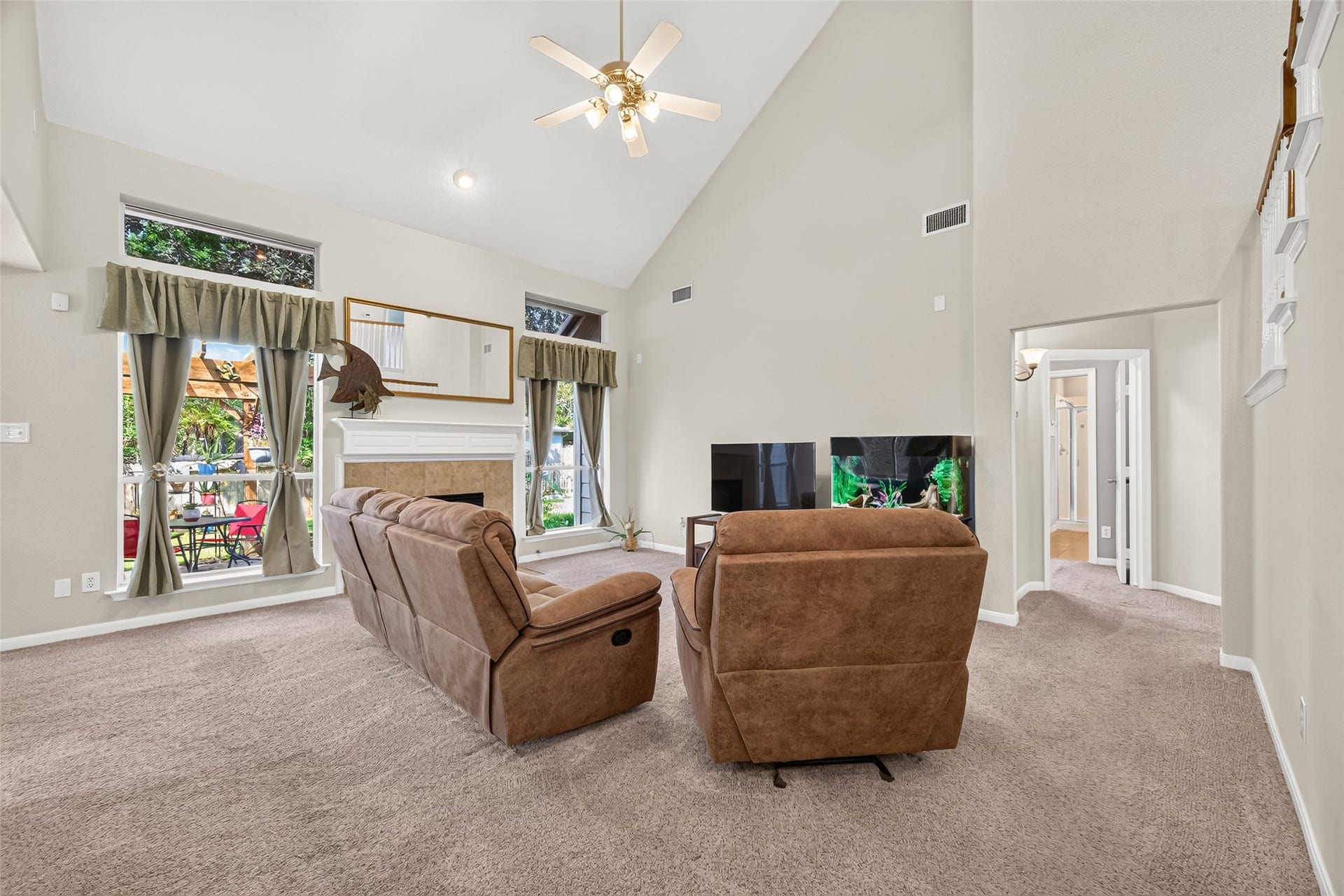 Spacious living room featuring soaring ceilings, a cozy fireplace, and large windows providing abundant natural light and backyard views.