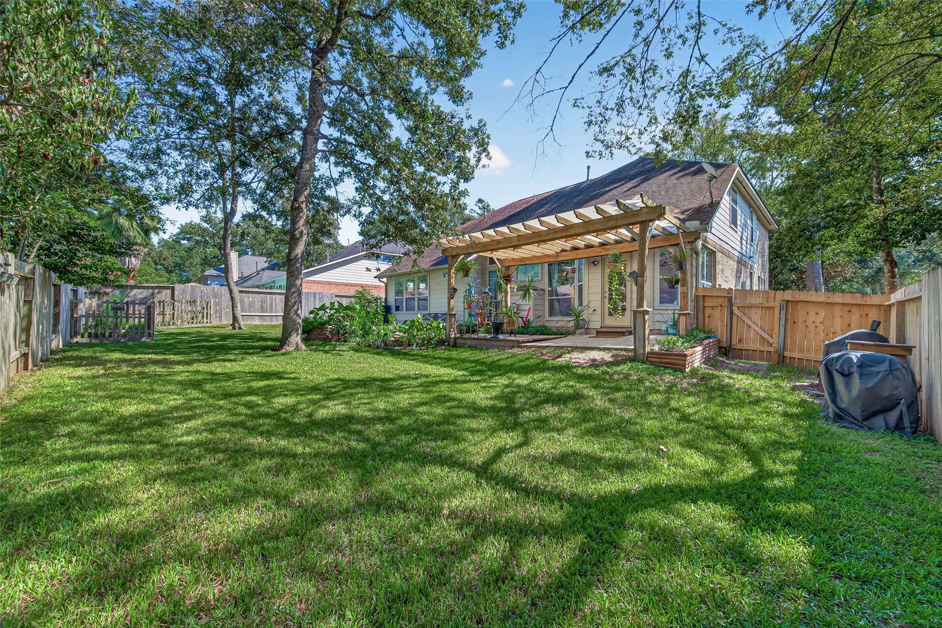 Spacious backyard featuring mature shade trees, established landscaping, and an inviting pergola-covered outdoor living area.