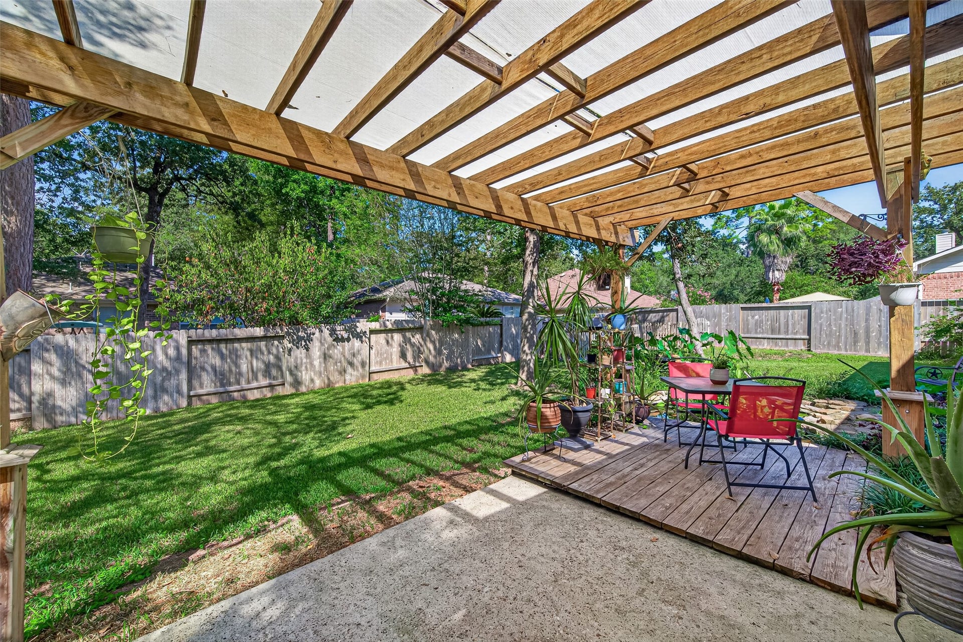 Inviting pergola-covered deck overlooking the spacious backyard, complemented by lush landscaping and a charming pond with a waterfall feature nearby.