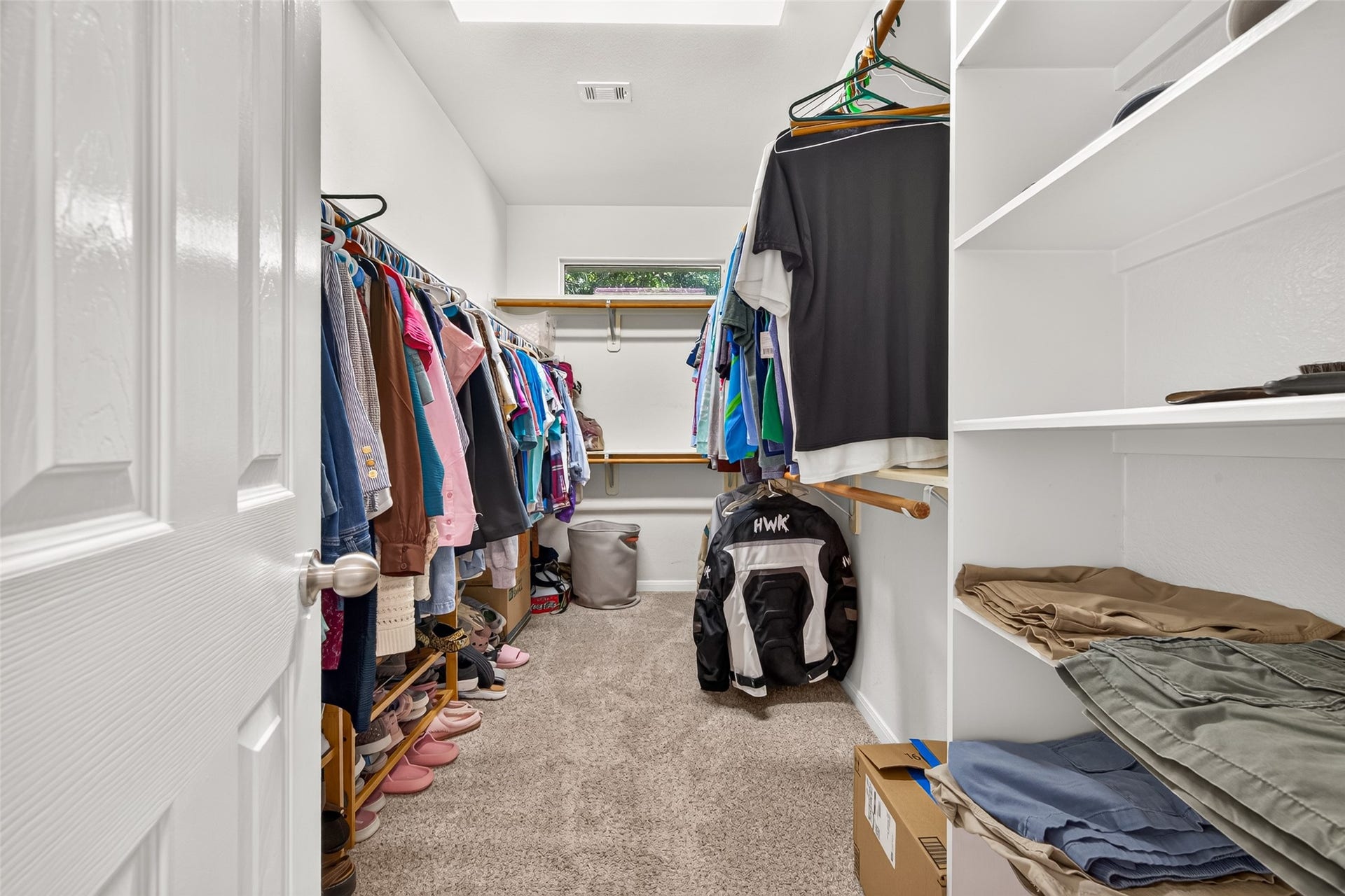 Spacious primary walk-in closet featuring multiple hanging areas, built-in shelving, and a window providing natural light.