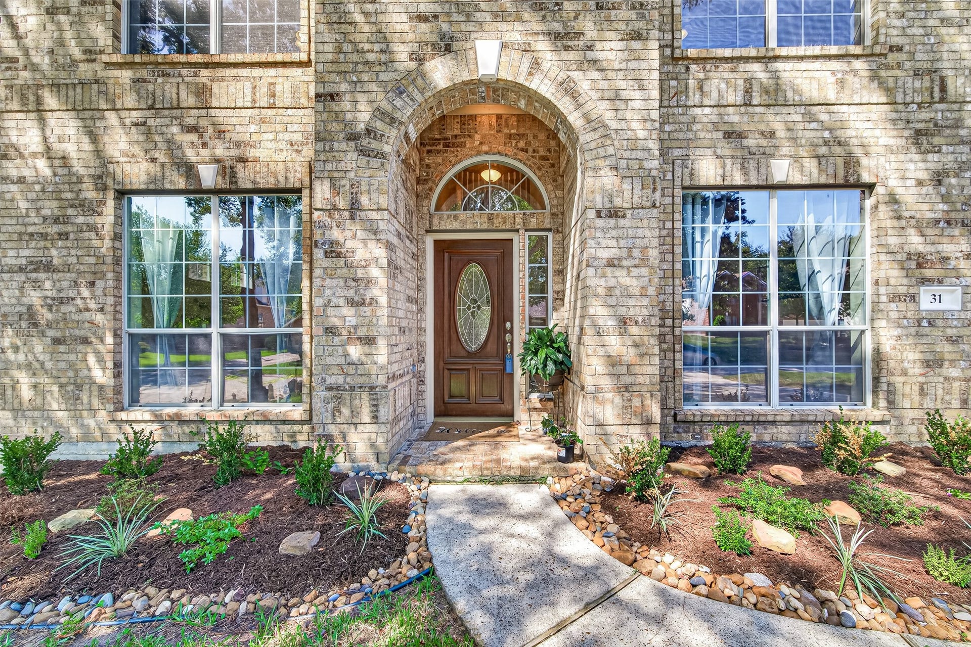 Welcoming covered entry featuring an elegant brick archway, decorative glass front door, and attractive landscaping.