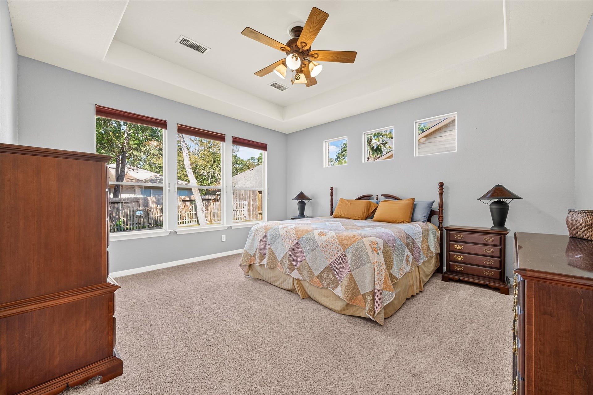 Spacious primary suite featuring a tray ceiling, ceiling fan, and abundant natural light from multiple windows overlooking the backyard.