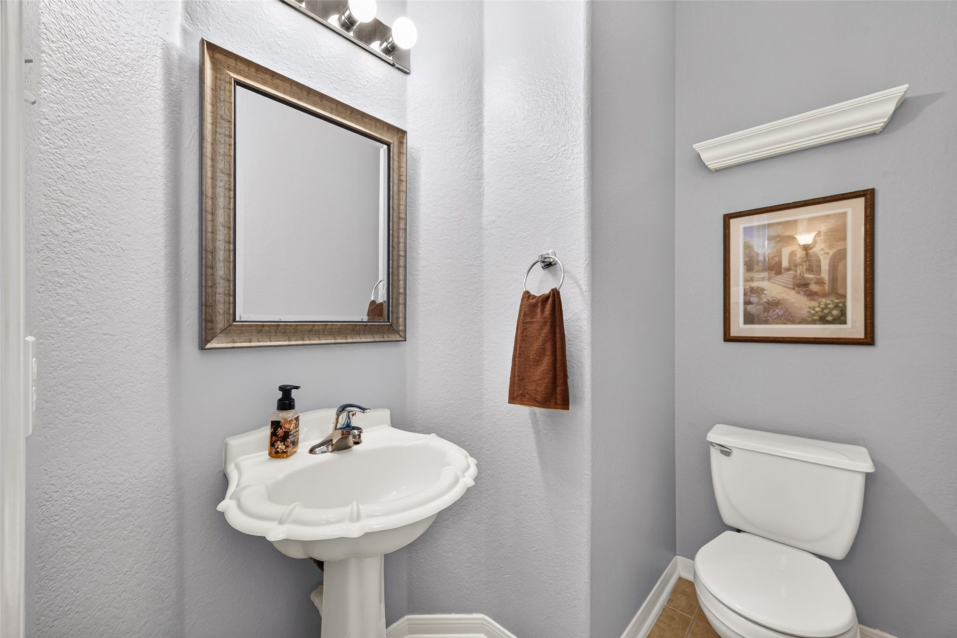 Conveniently located half bath just off the living room, ideal for guests. Featuring a decorative pedestal sink, framed mirror, and neutral finishes.