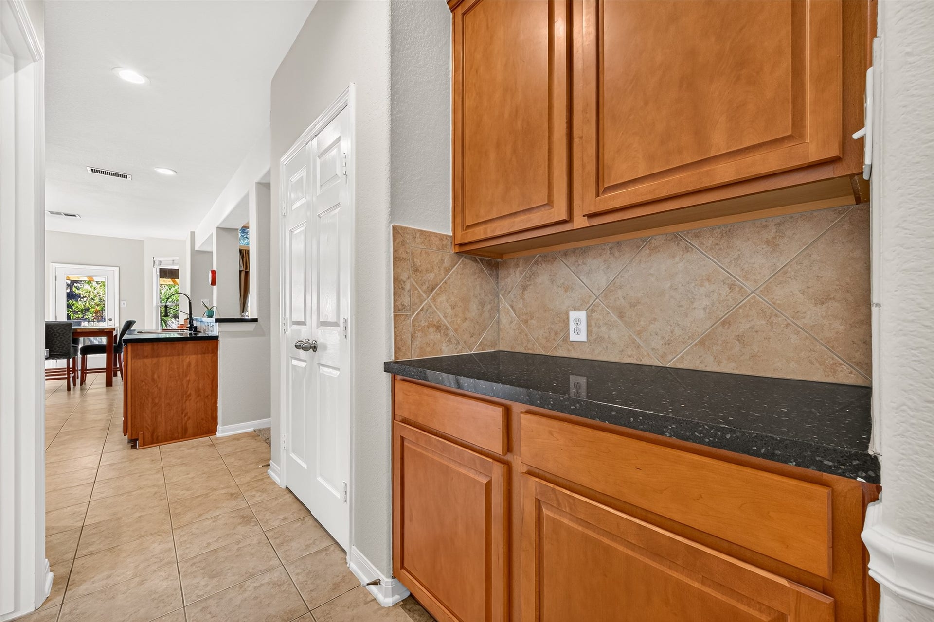 Convenient butler's pantry featuring additional cabinetry, generous counter space, and a coordinating tile backsplash for extra storage and serving space.